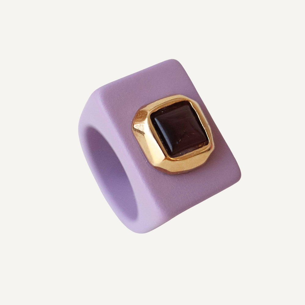 Anillo cuadrado de silicona morada con detalle dorado y piedra marrón. Estilo moderno y llamativo.