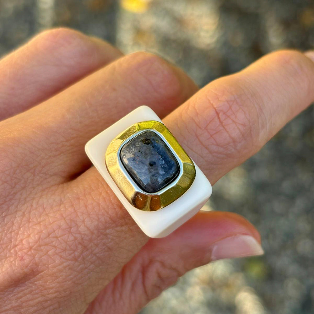 Anillo de resina blanca con piedra azul y detalles dorados, estilo moderno y elegante.