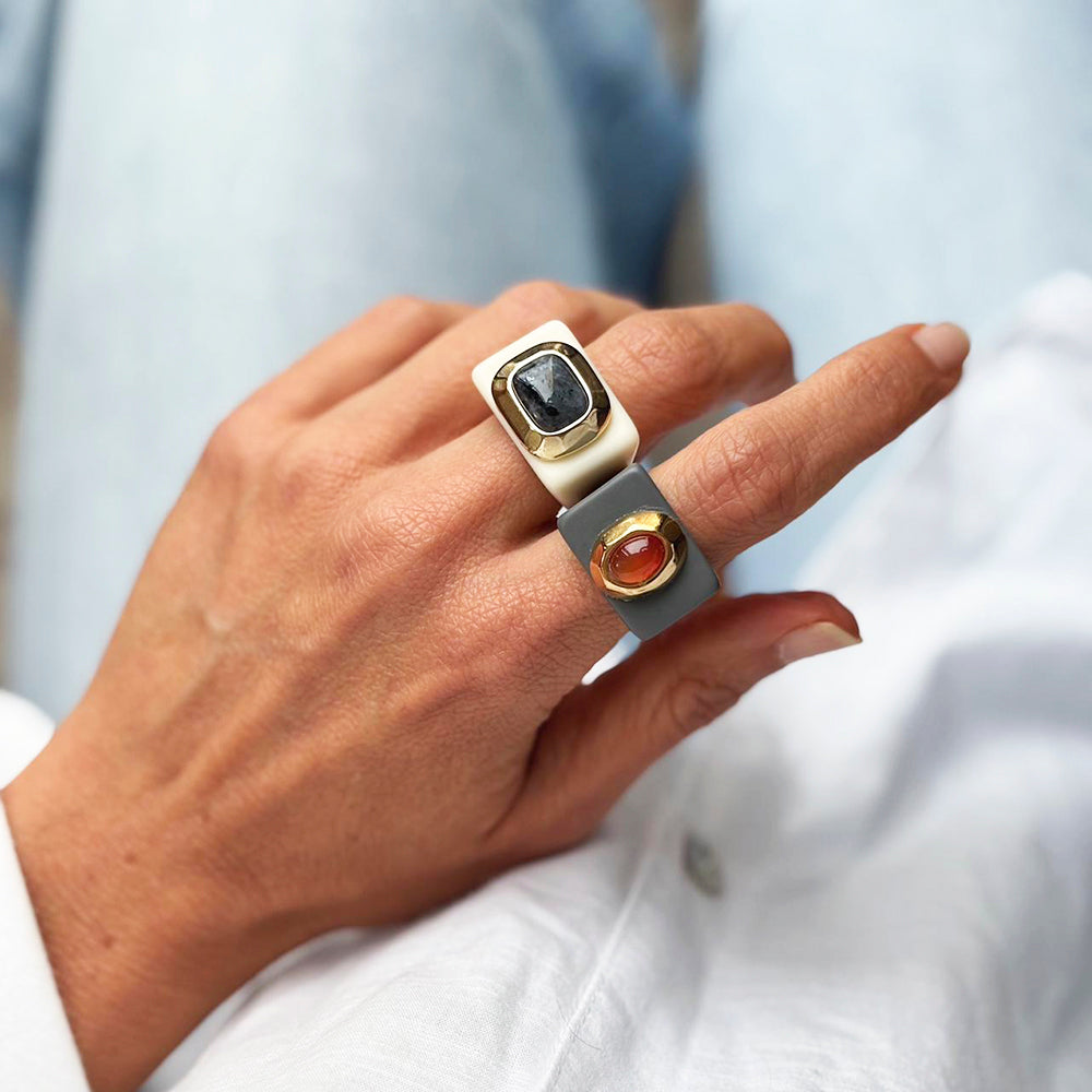 Anillo moderno de resina gris con gemas negras y naranjas, elegante y minimalista, ideal para un look contemporáneo.