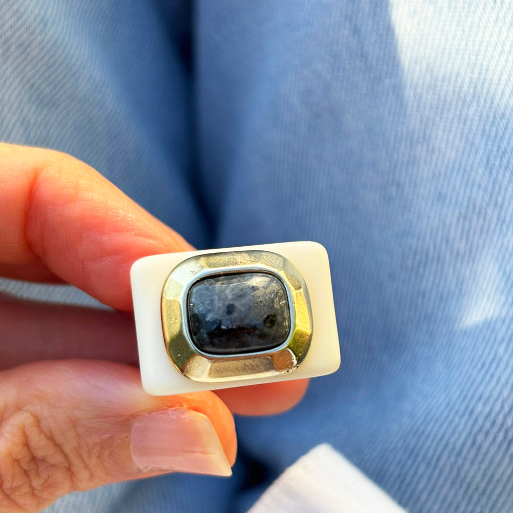 Anillo con piedra negra y base dorada, diseño moderno, material cerámico y metálico.