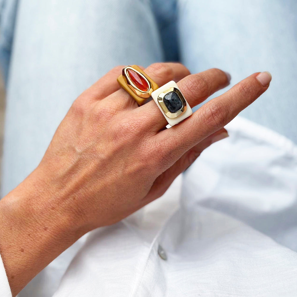 Anillo dorado y anillo blanco con piedras rojas y negras, estilo moderno, sobre mano con jeans claros.