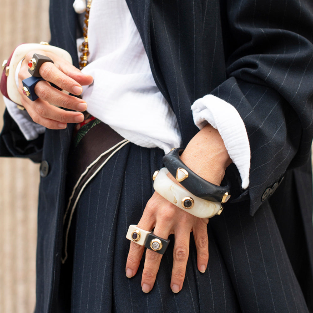Pulseras de resina y anillos en negro, blanco y dorado con detalles geométricos, estilo moderno.
