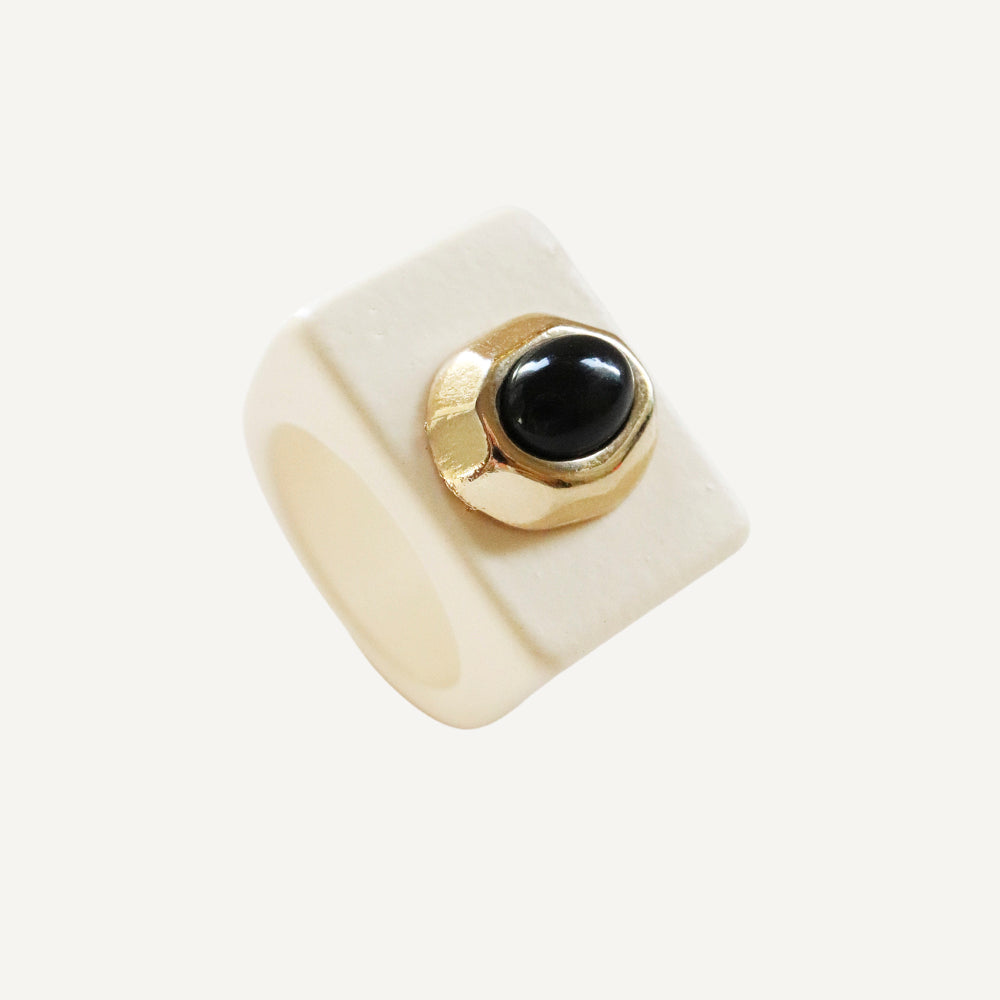 Anillo cuadrado blanco con detalle dorado y gema negra, elegante y moderno.