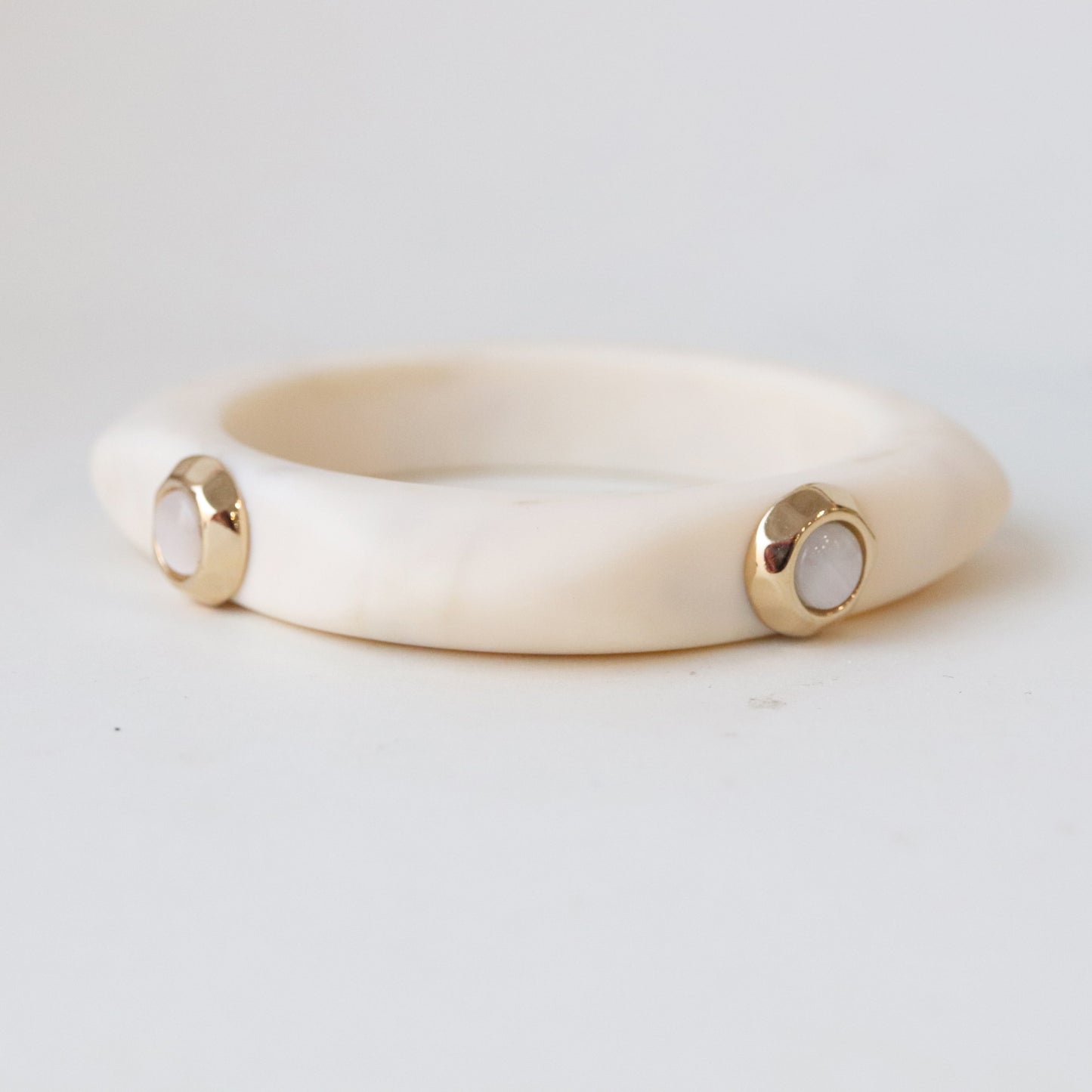 Pulsera de resina blanca con detalles dorados y piedras pink, diseño moderno y elegante.