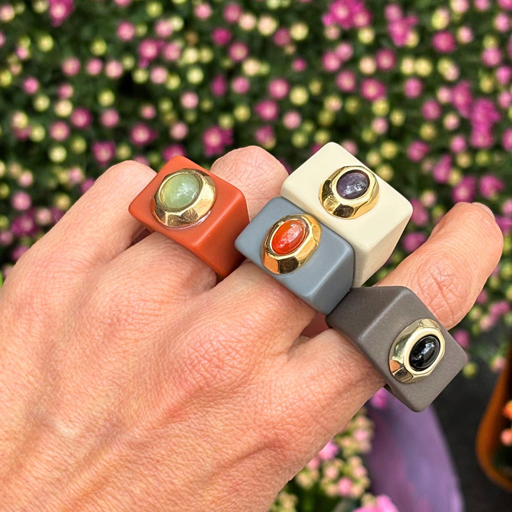 Anillos de resina en tonos terracota, gris, beige y verde, con gemas y detalle dorado.