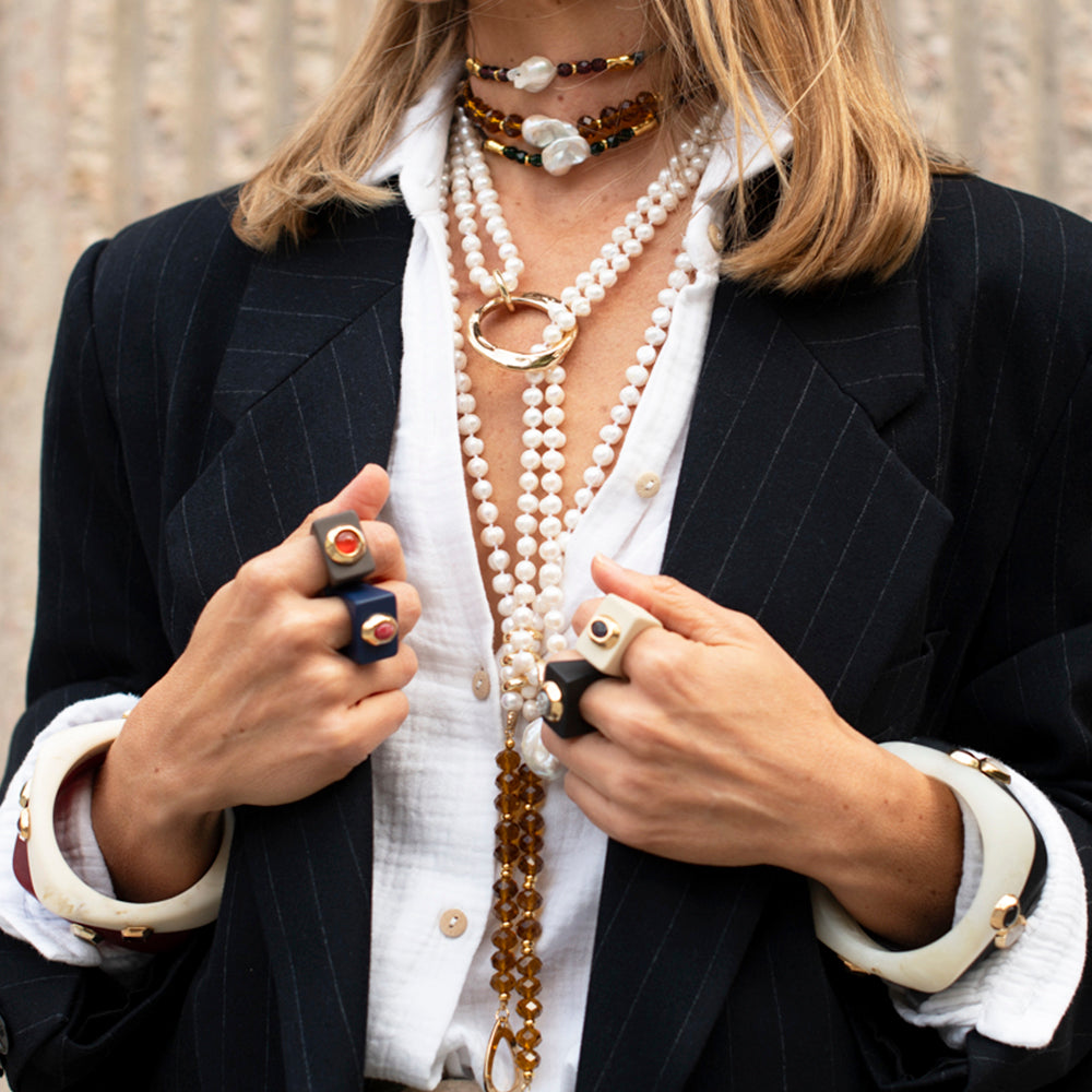 Collares de perlas y ámbar con anillos y brazaletes en estilo elegante, sobre blazer a rayas negro.