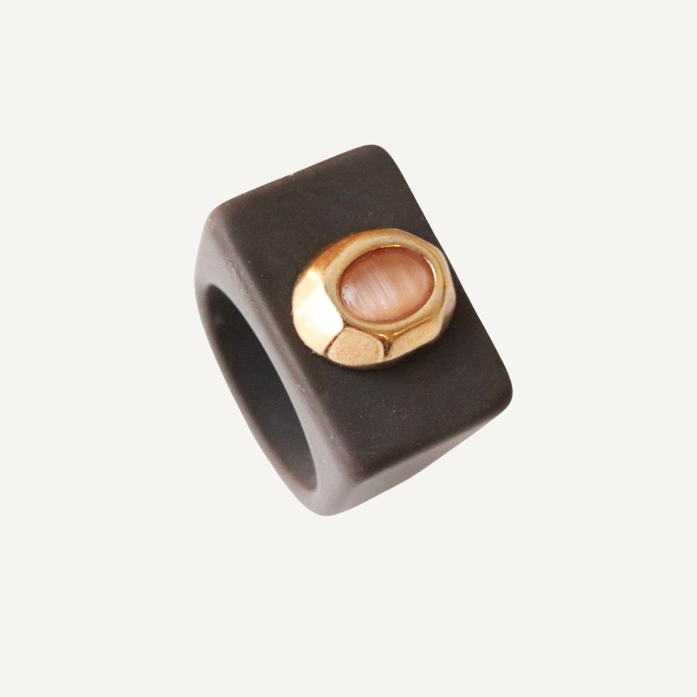 Anillo negro de cerámica con detalle dorado y piedra rosa, diseño moderno y minimalista.