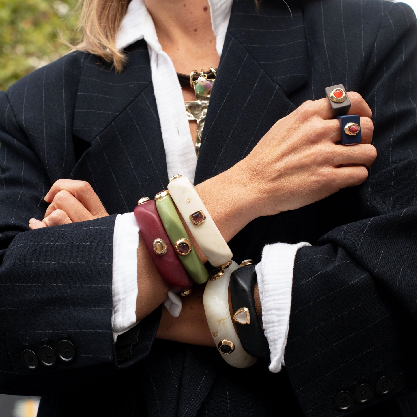 Brazaletes de varios colores (verde, rojo, blanco, negro) y anillos de estilo elegante en modelo con blazer a rayas.
