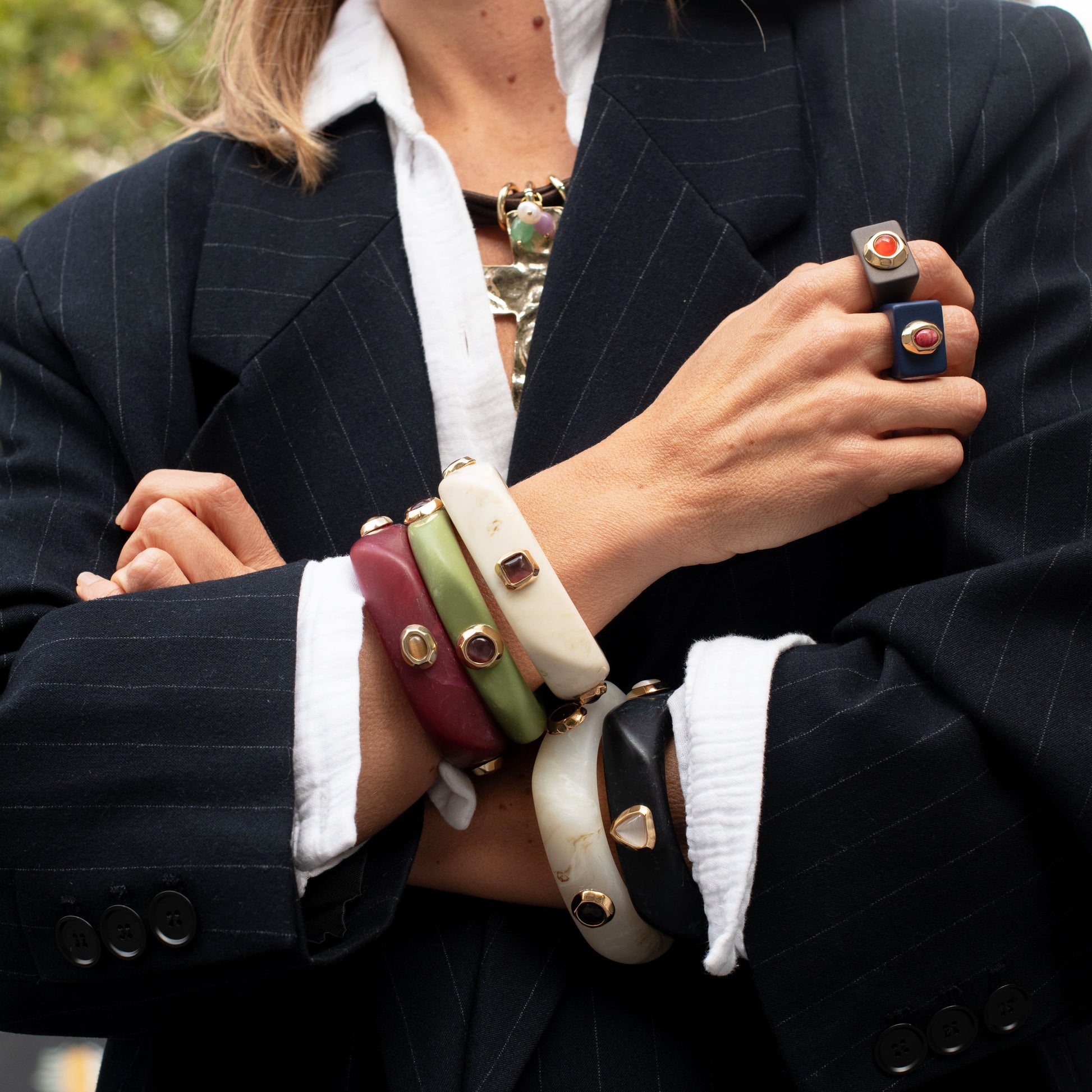 Brazaletes de varios colores (verde, rojo, blanco, negro) y anillos de estilo elegante en modelo con blazer a rayas.
