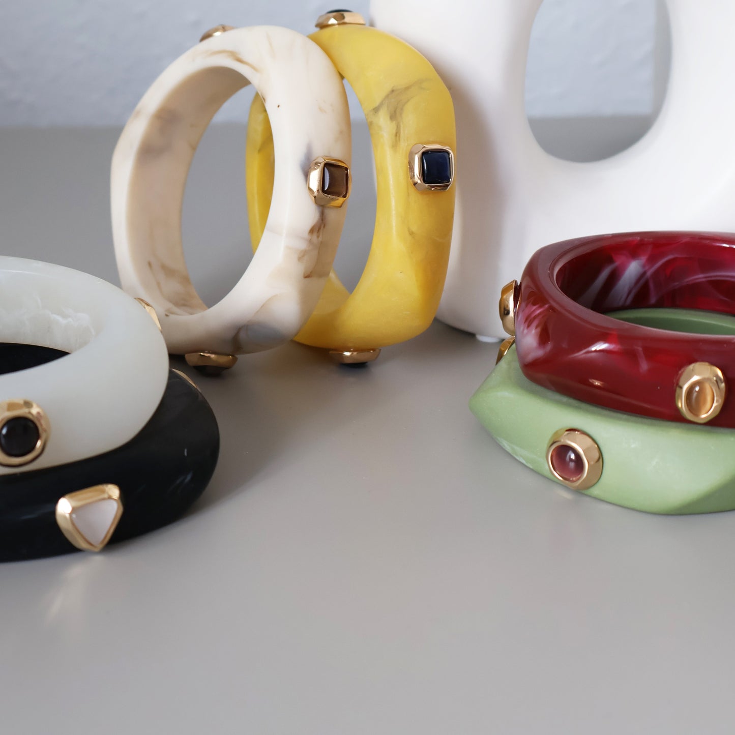 Brazaletes de resina en blanco, negro, amarillo, rojo y verde, con detalles dorados y piedras decorativas.