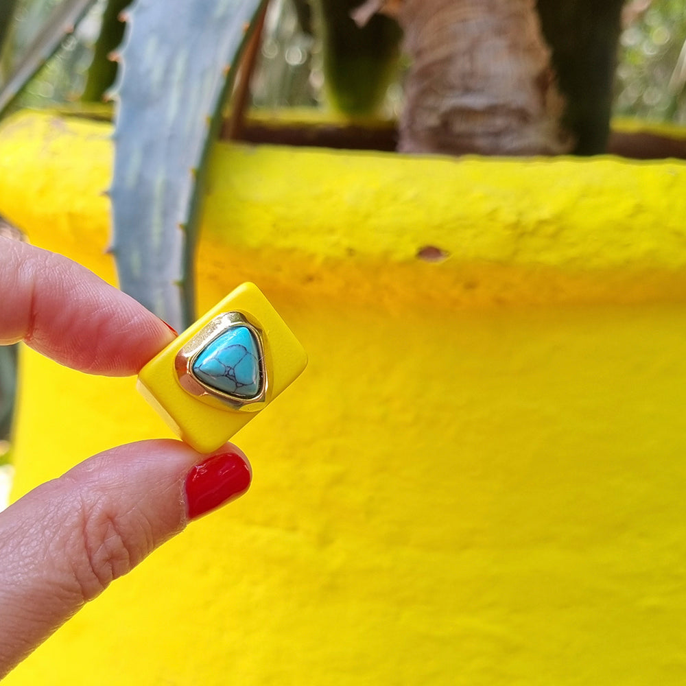 Anillo amarillo con piedra turquesa en forma triangular, estilo moderno y llamativo.