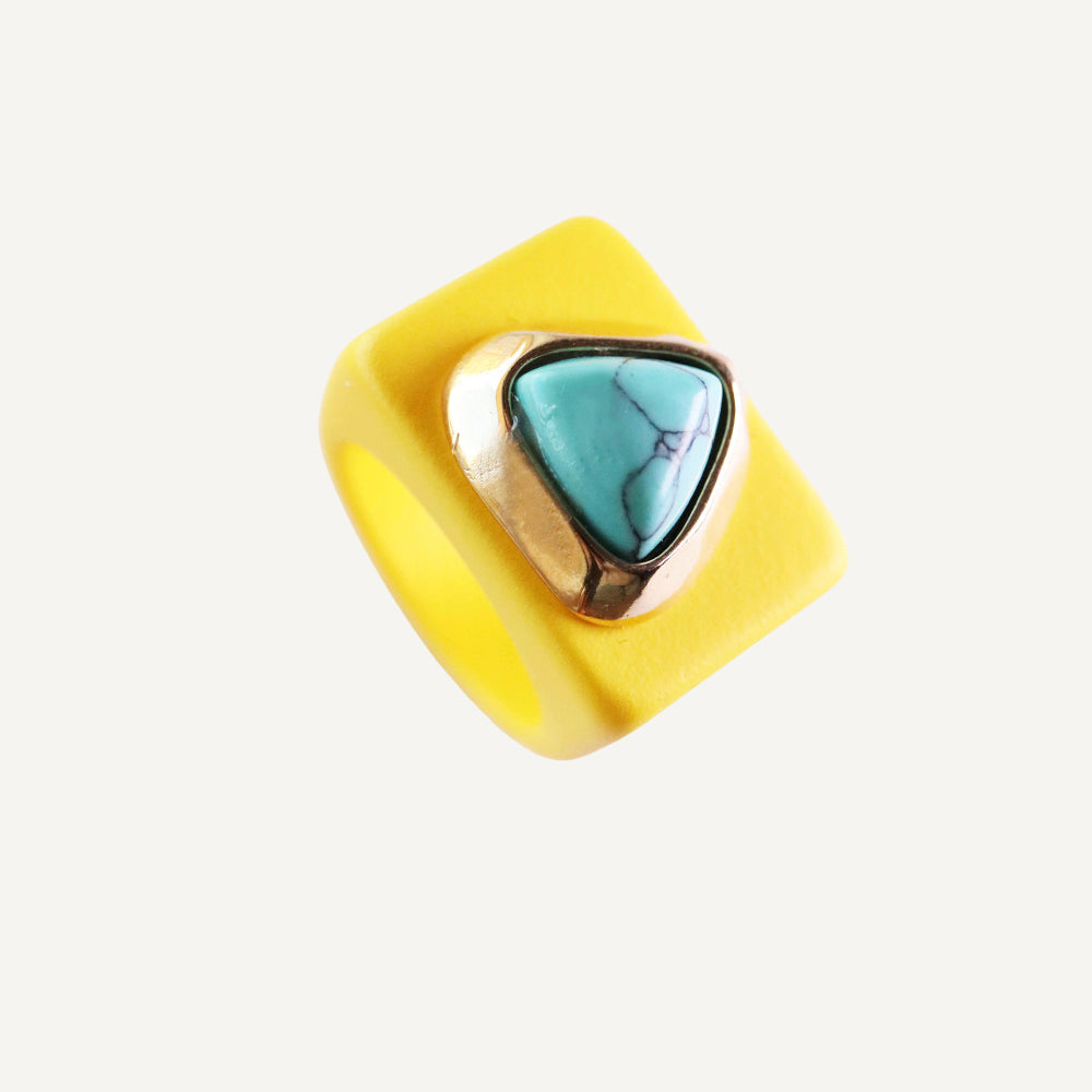 Anillo amarillo de resina con piedra turquesa en forma de triángulo y acabado dorado.