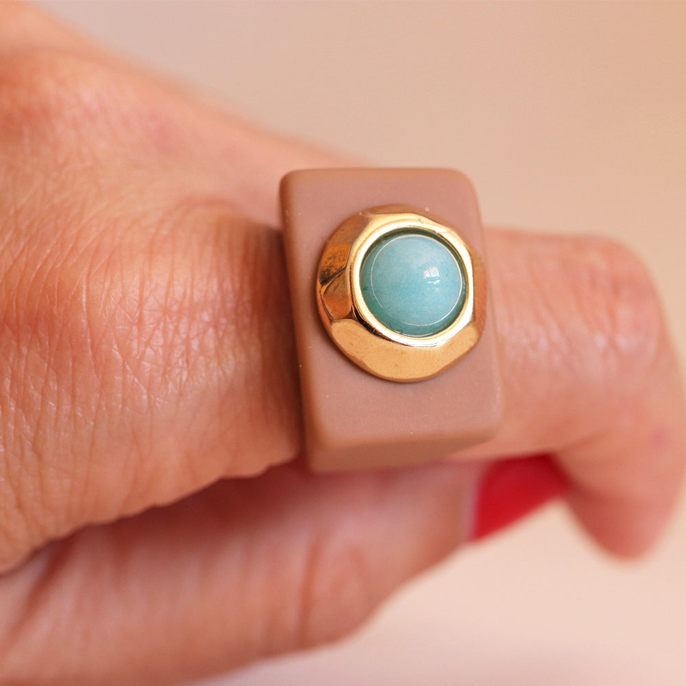 Anillo de resina beige con piedra azul y detalle dorado, diseño moderno y elegante.