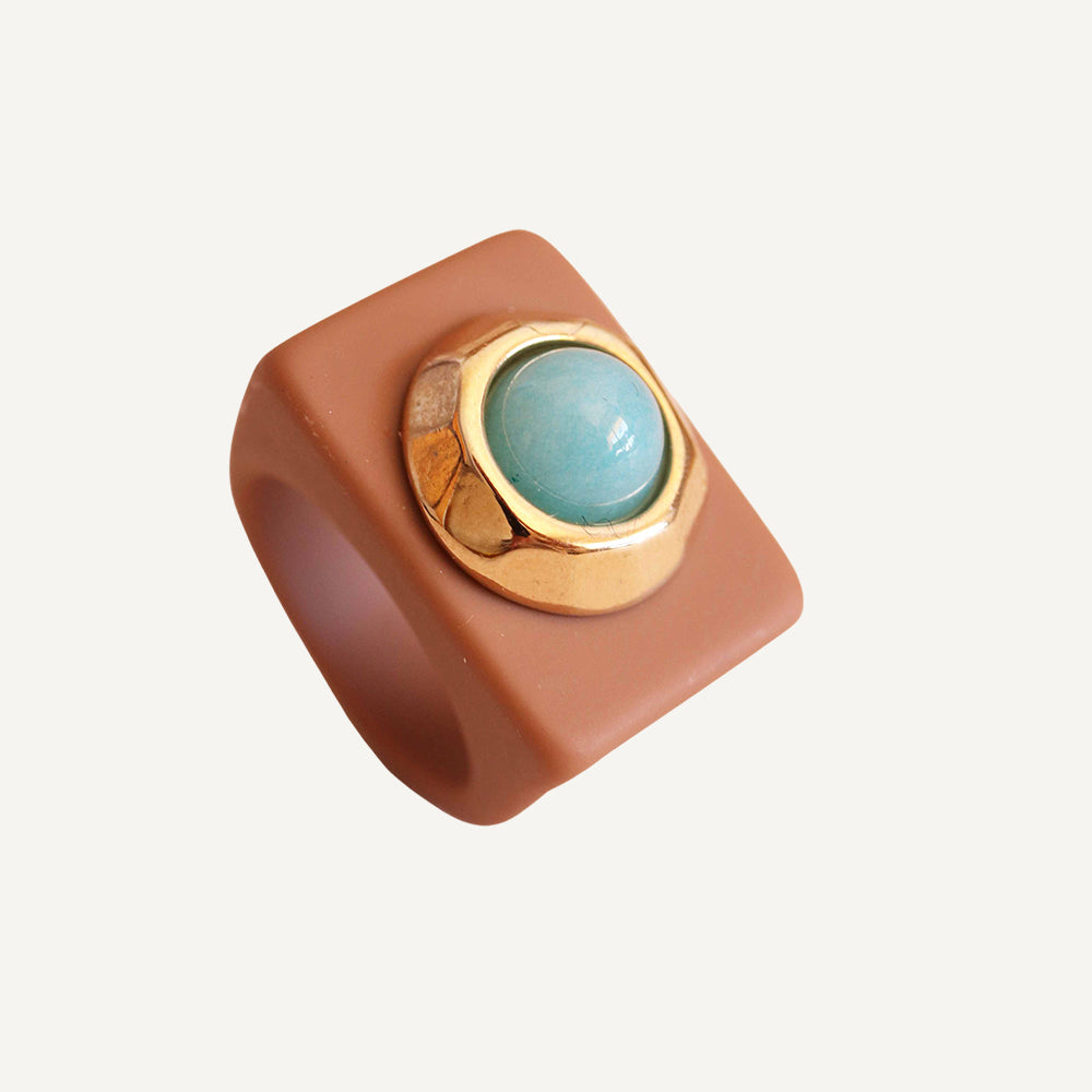 Anillo de silicona marrón con piedra azul y detalles dorados, estilo moderno y elegante.