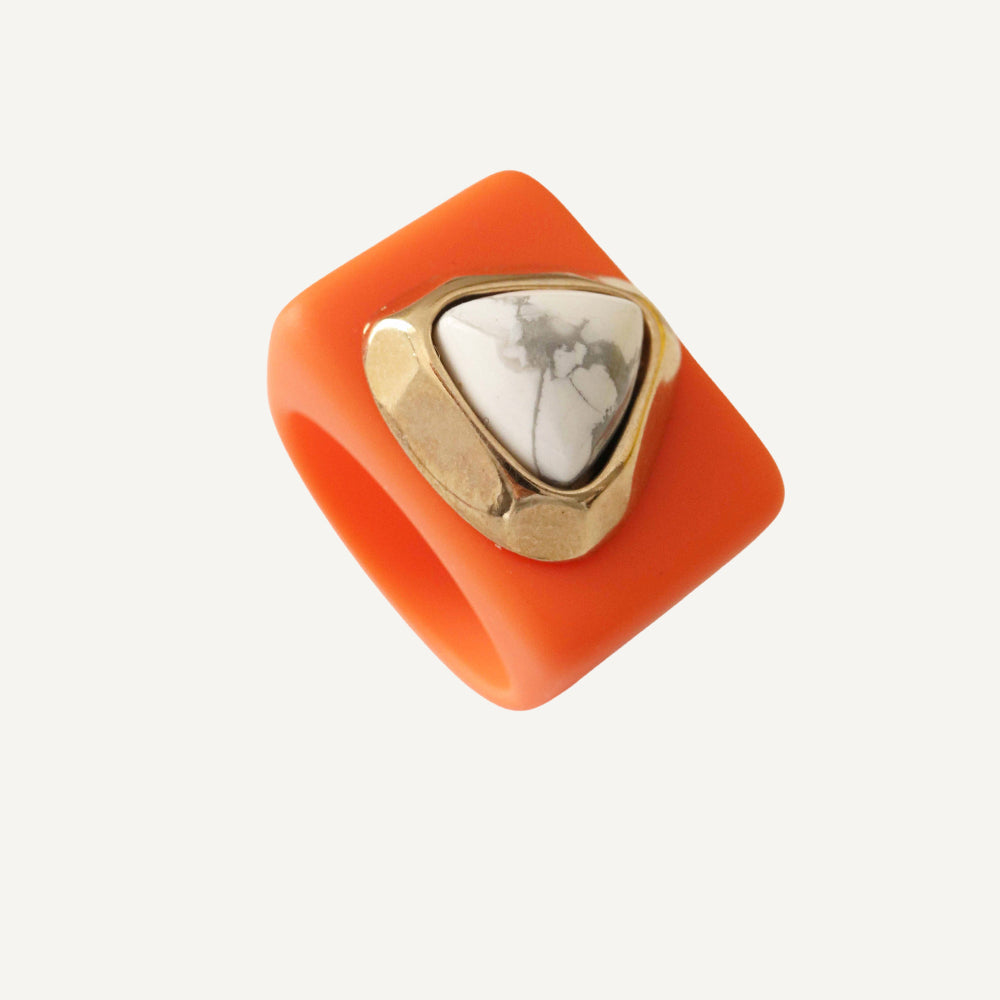 Anillo de resina naranja con piedra blanca y dorado, estilo moderno y llamativo.