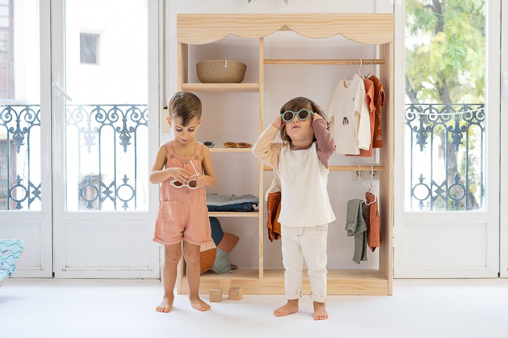 Conjunto de ropa infantil con tonos pastel, madera clara y estilo moderno en habitación luminosa.