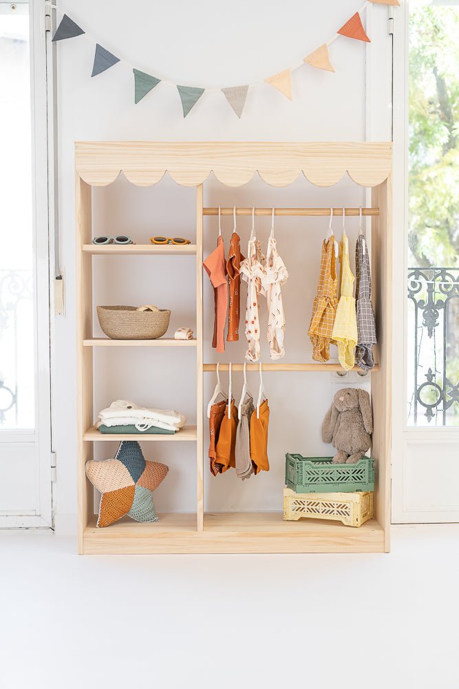 Estante de madera claro con ropa infantil en tonos mostaza y terracota, decoración colorida y estilo minimalista.