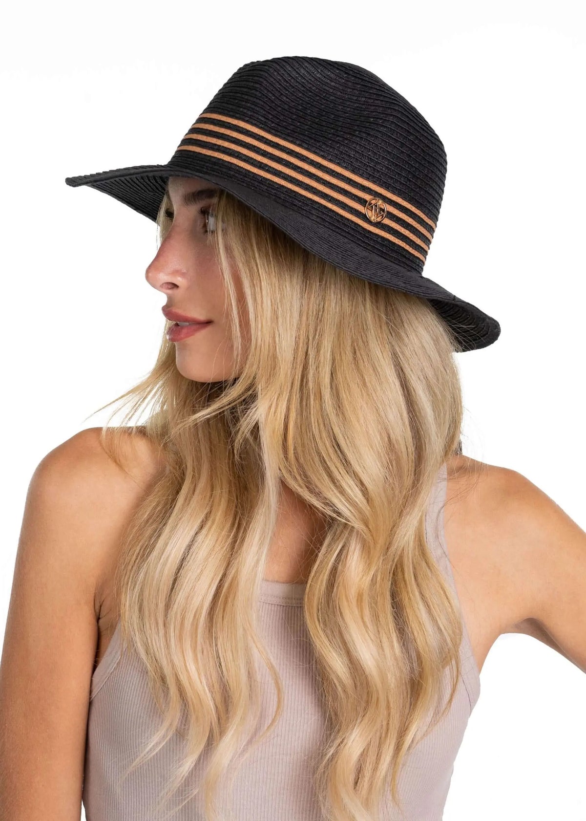 Black straw Panama hat with tan striped band and gold logo emblem, worn by a blonde model.