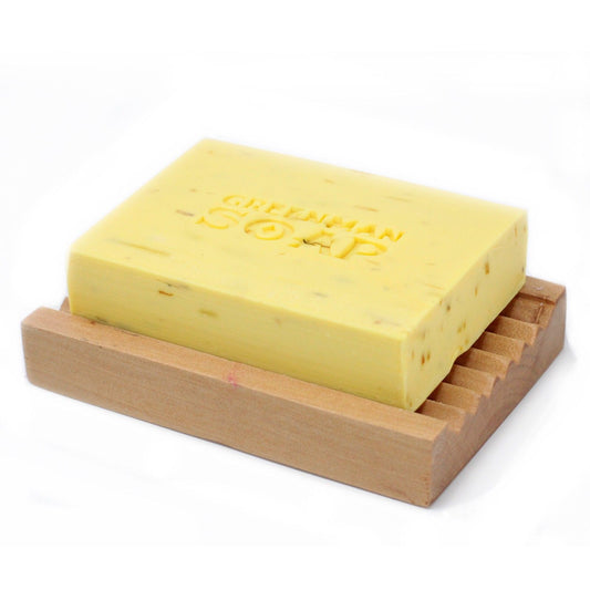 Jabón rectangular amarillo con textura, marcado "GREENMAN SOAP", sobre una jabonera de madera acanalada. Fondo blanco.