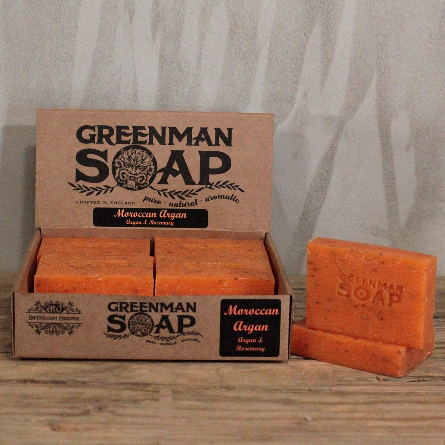 Caja de cartón con jabones naranja texturizados de argán Greenman. Logo de rostro natural y estilo rústico artesanal.