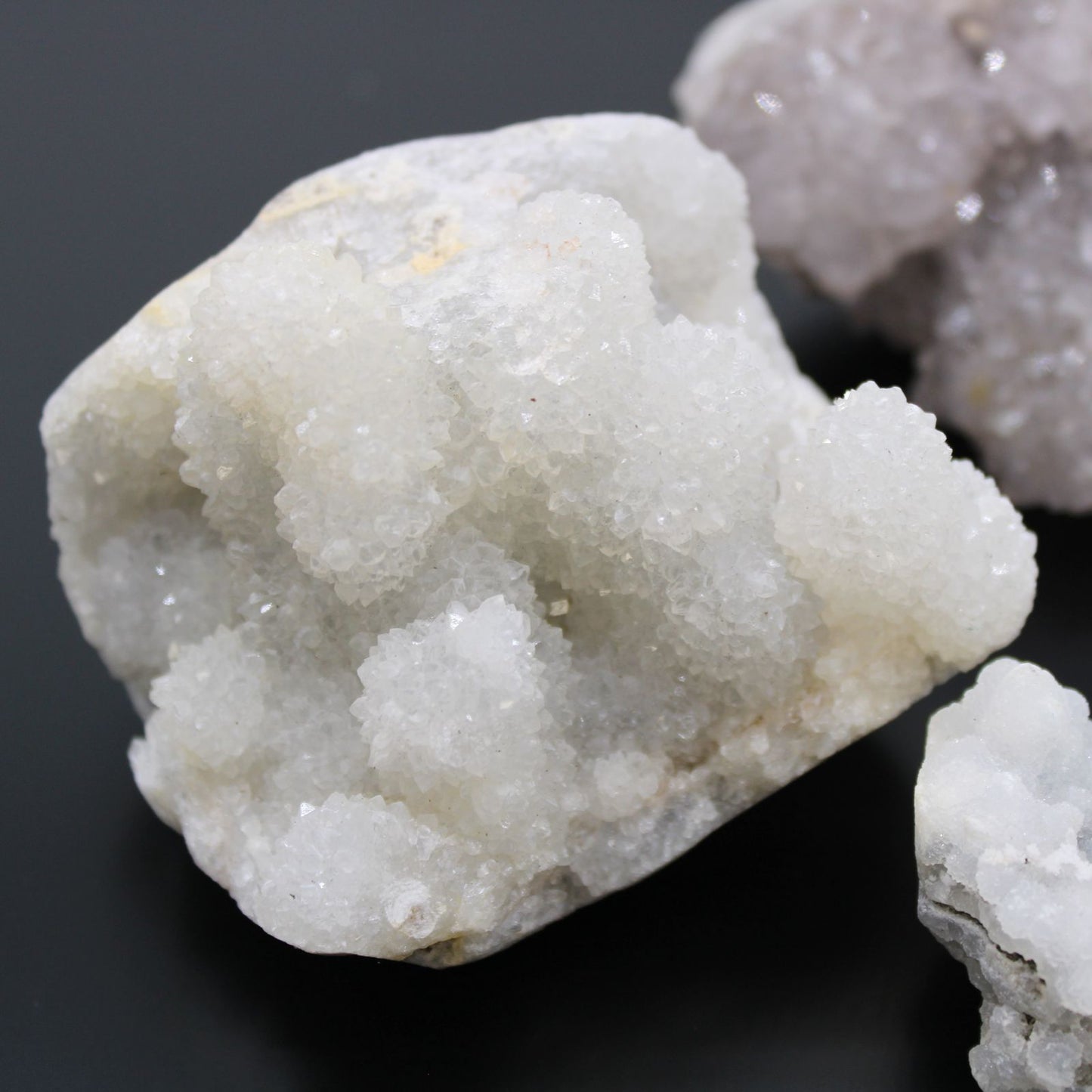 Cristal de cuarzo blanco brillante, rugoso, con textura granulada y destellos sutiles sobre fondo oscuro.