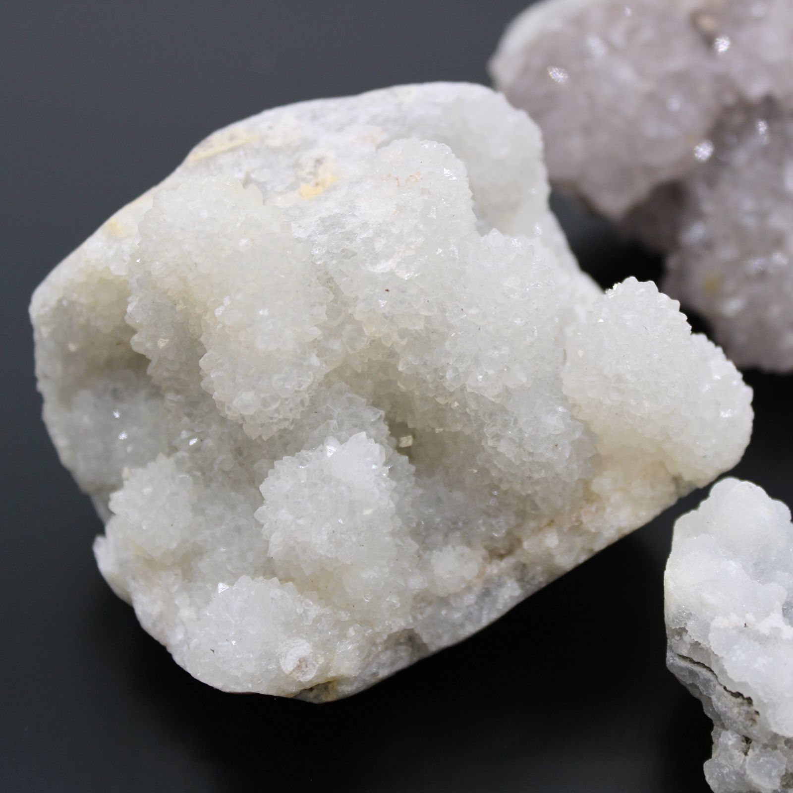 Cristal de cuarzo blanco brillante, rugoso, con textura granulada y destellos sutiles sobre fondo oscuro.