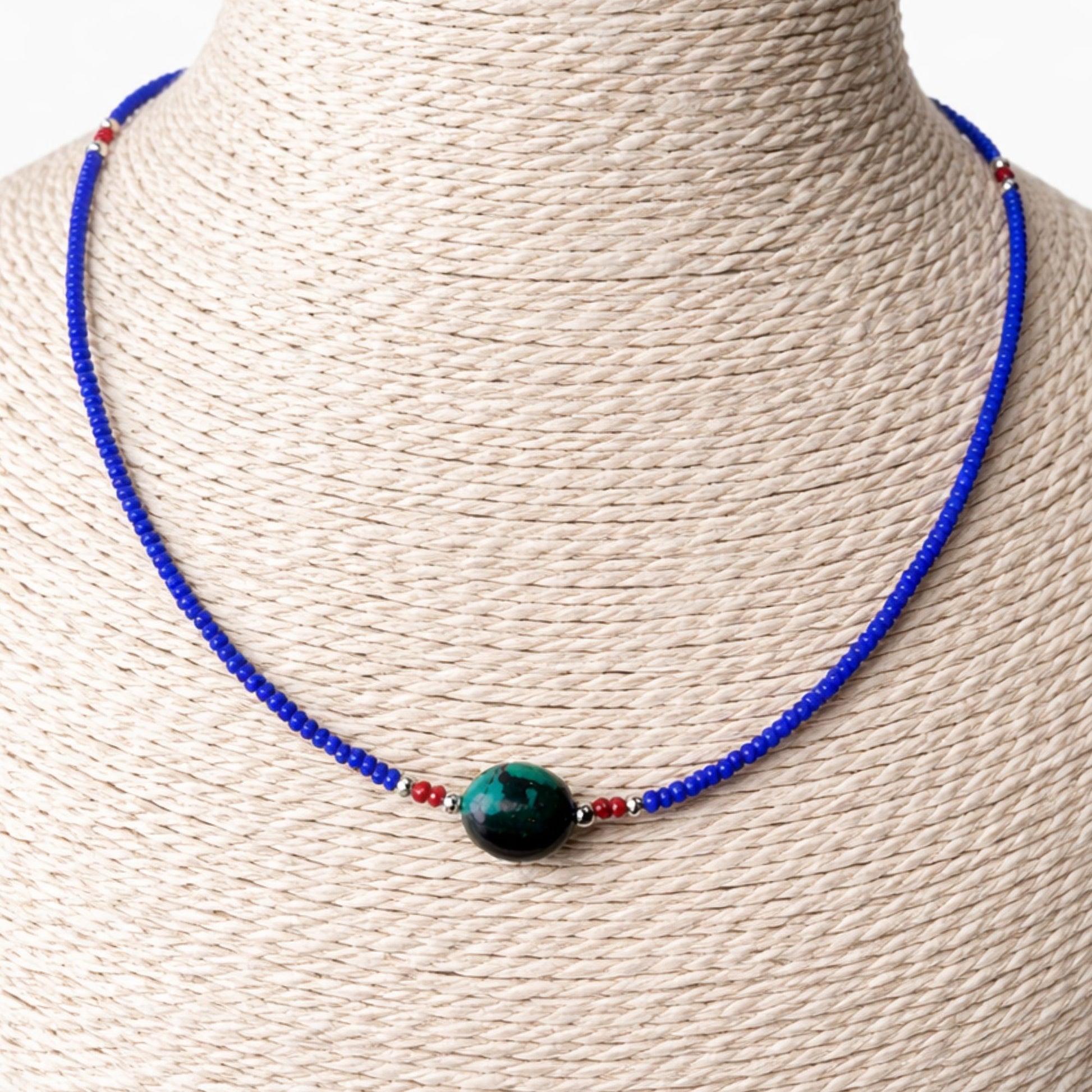 Collar de cuentas azules y rojas con un ópalo verde, estilo bohemio, ideal para ocasiones casuales.