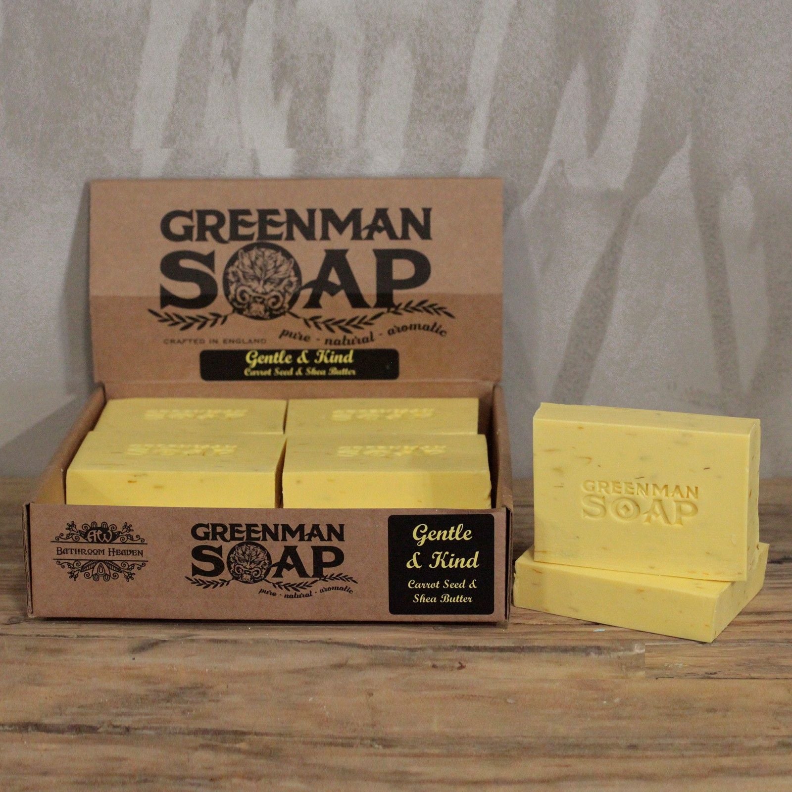 Caja de cartón con pastillas de jabón amarillas, marca Greenman "Gentle & Kind", sobre mesa de madera.