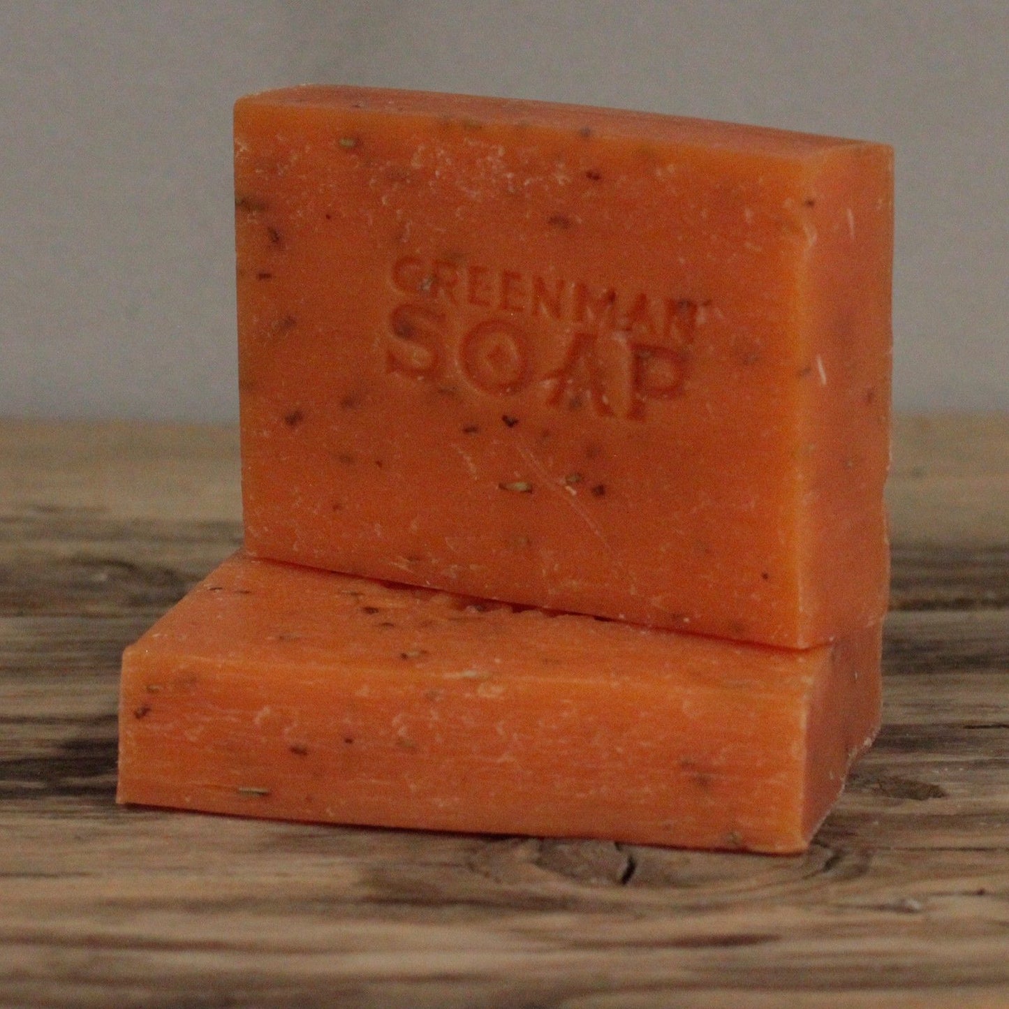 Dos pastillas de jabón naranja con motas, marcadas como "Greenman Soap", sobre una superficie de madera rústica.