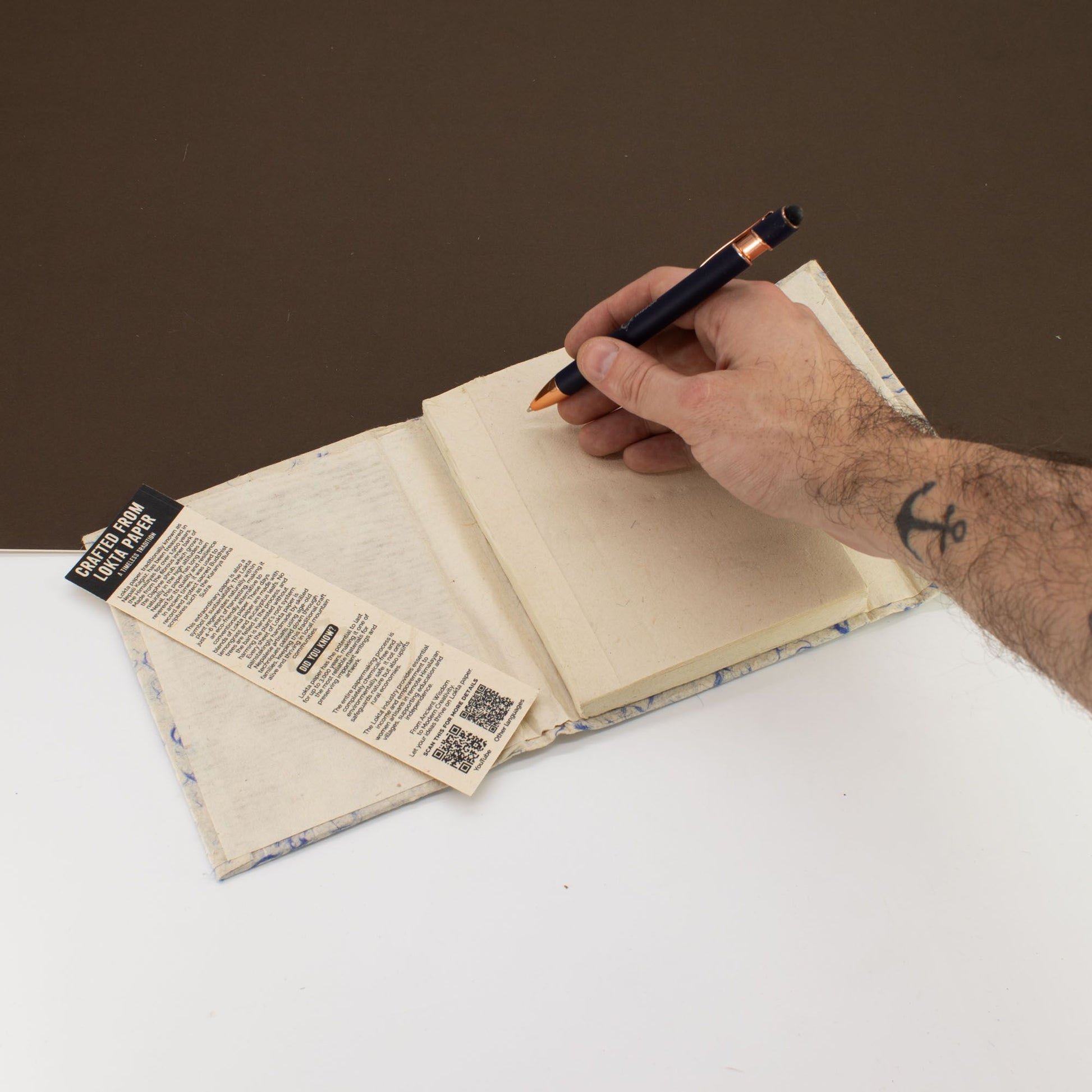 Cuaderno de papel reciclado con portada azul, escritura a mano con lápiz negro en fondo blanco y marrón.