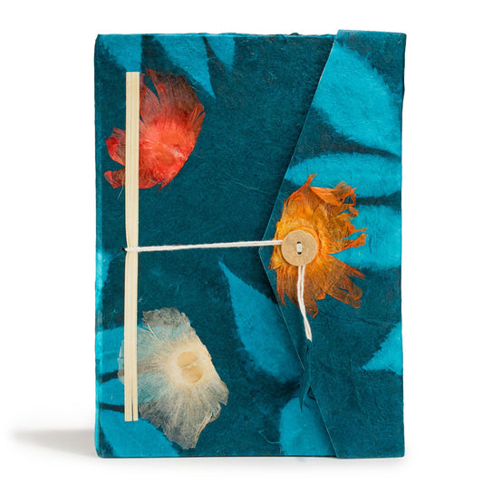 Cuaderno artesanal de papel reciclado azul con flores secas en tonos rojos y naranjas, atado con cuerda natural.