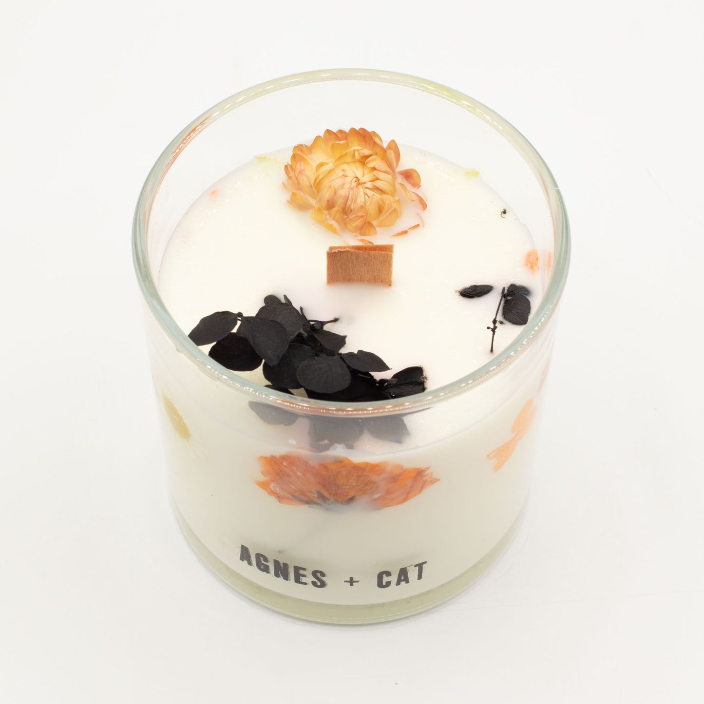 Vela aromática blanca con flores secas naranjas y negro, en frasco de vidrio, estilo elegante y moderno.