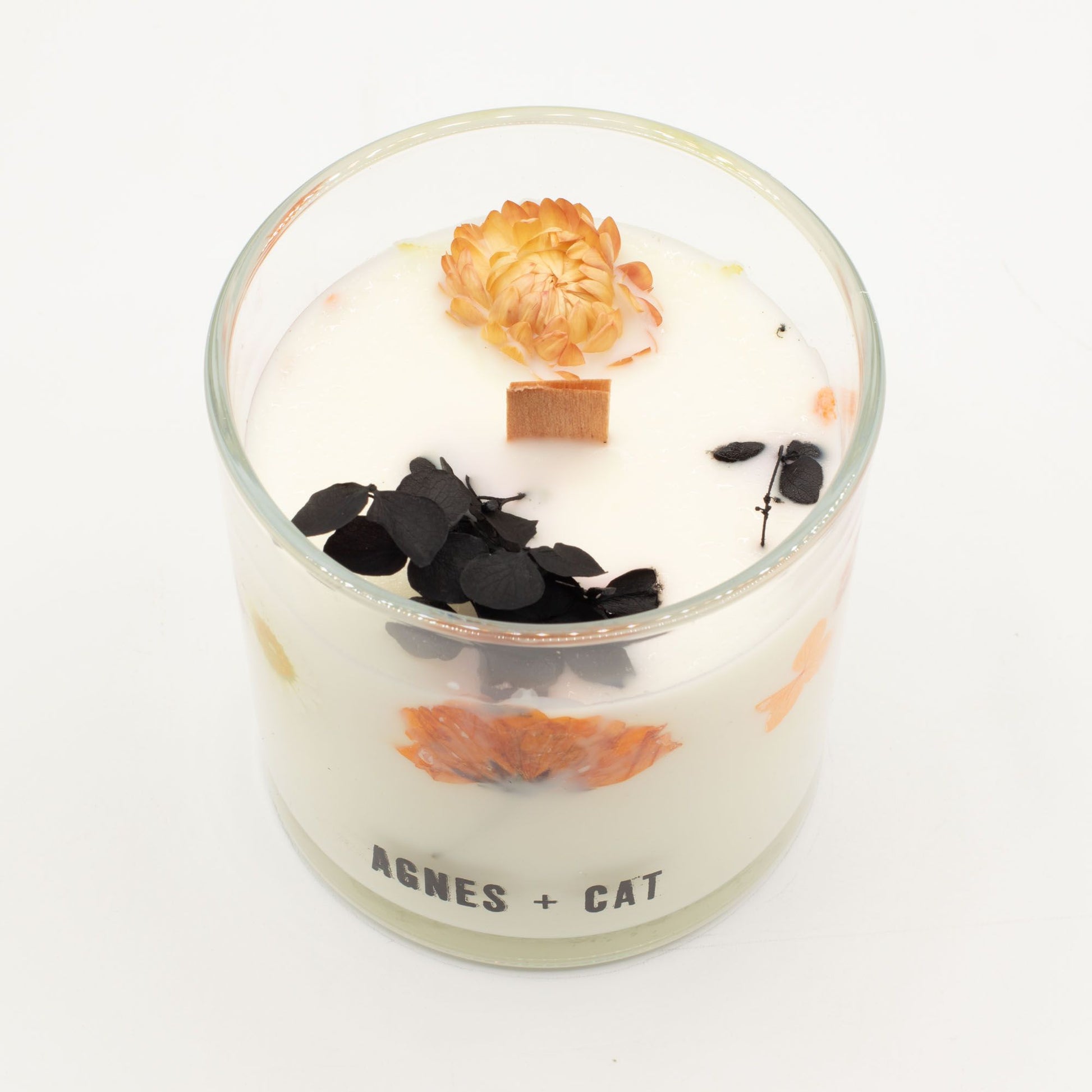 Vela aromática blanca con flores secas naranjas y negro, en frasco de vidrio, estilo elegante y moderno.