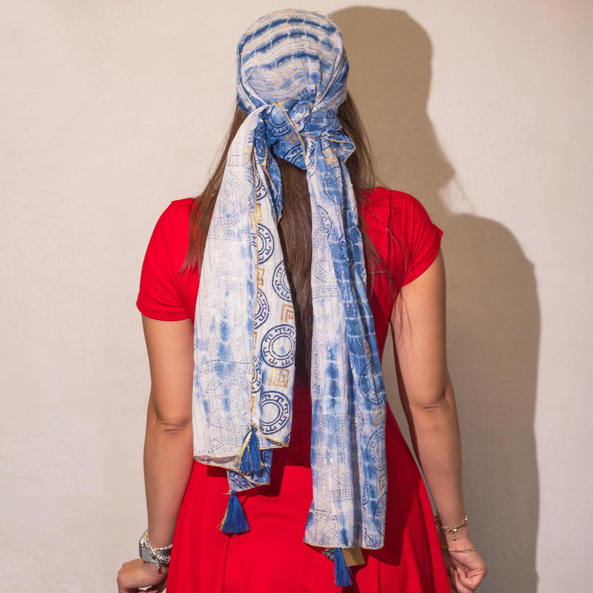 Pañuelo azul de algodón con estampado tribal, ideal como accesorio de moda, atado con flecos en un vestido rojo.