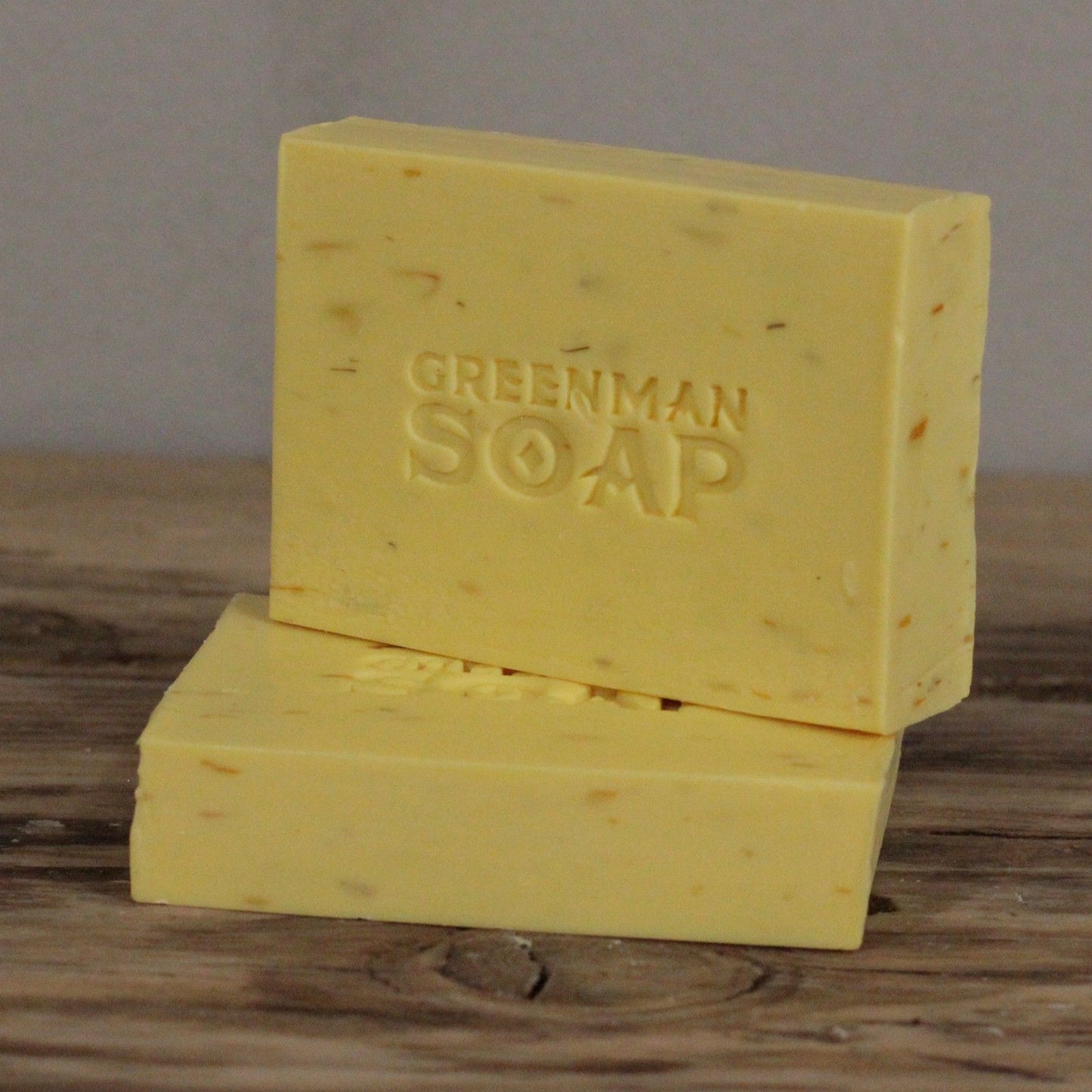 Dos pastillas de jabón amarillas, una sobre otra, con textura rústica y la inscripción "GREENMAN SOAP" en relieve.