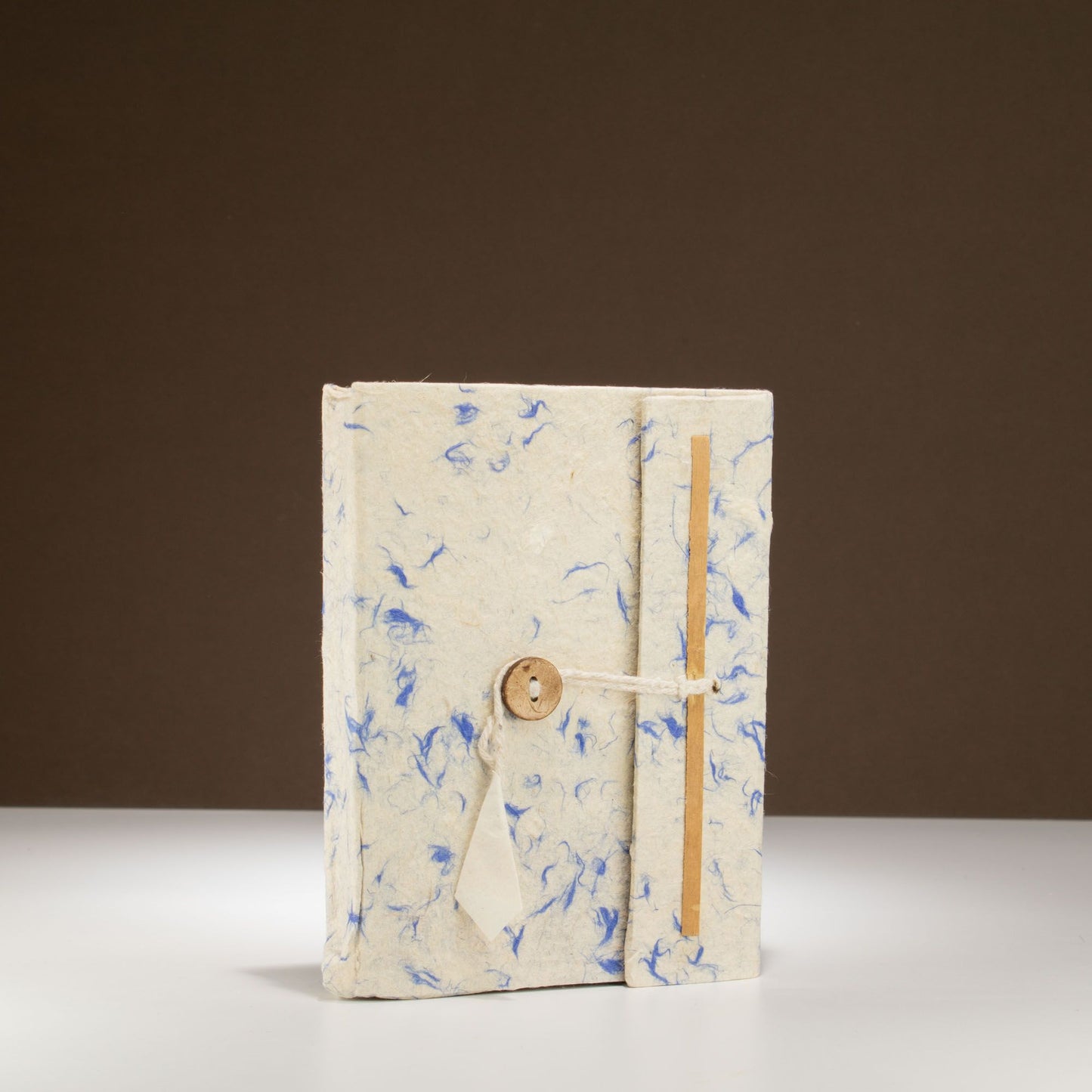 Cuaderno artesanal de papel reciclado, color blanco con detalles azules y cierre de cuerda y botón de madera.