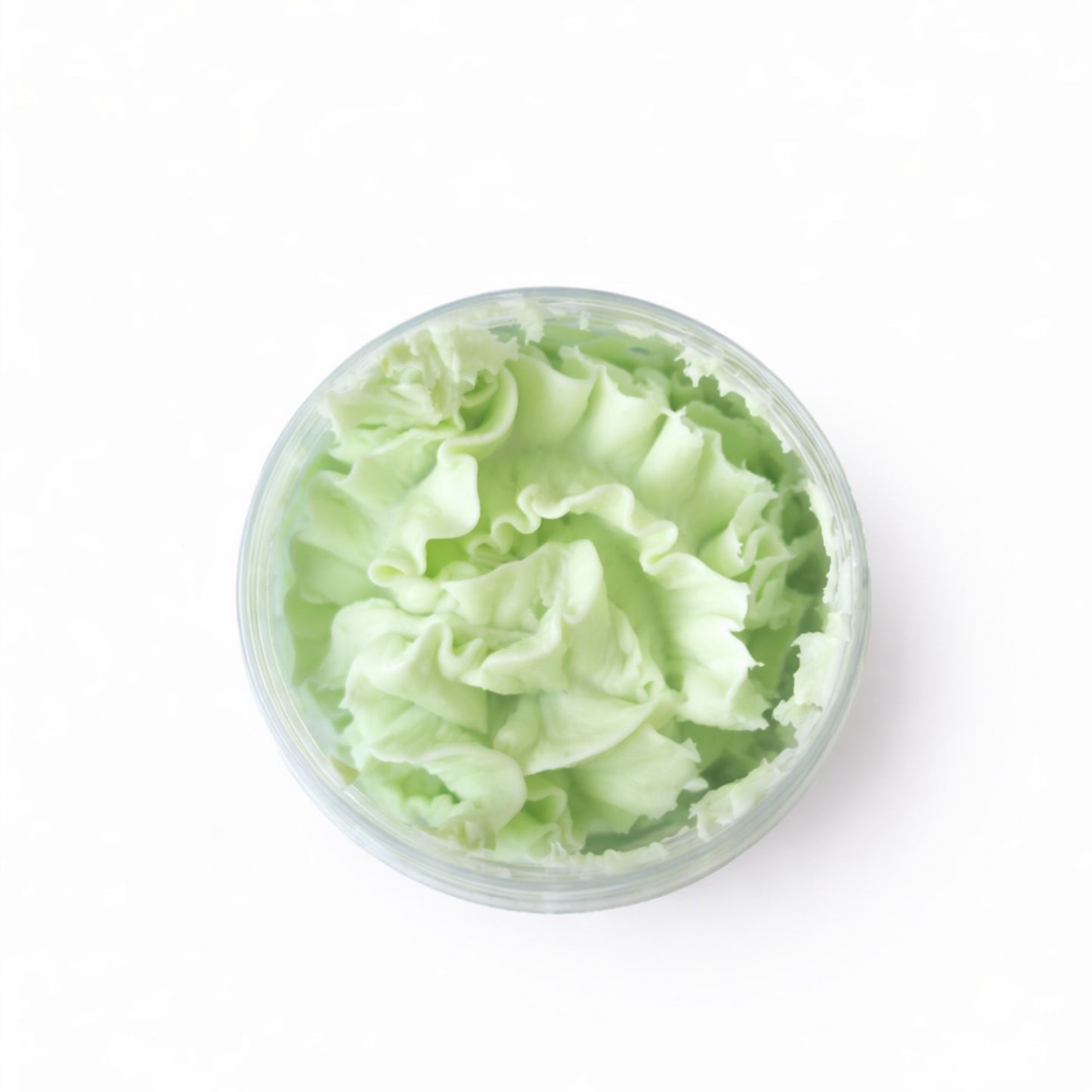 Crema facial de color verde menta en recipiente transparente, textura suave y esponjosa, ideal para hidratar la piel.