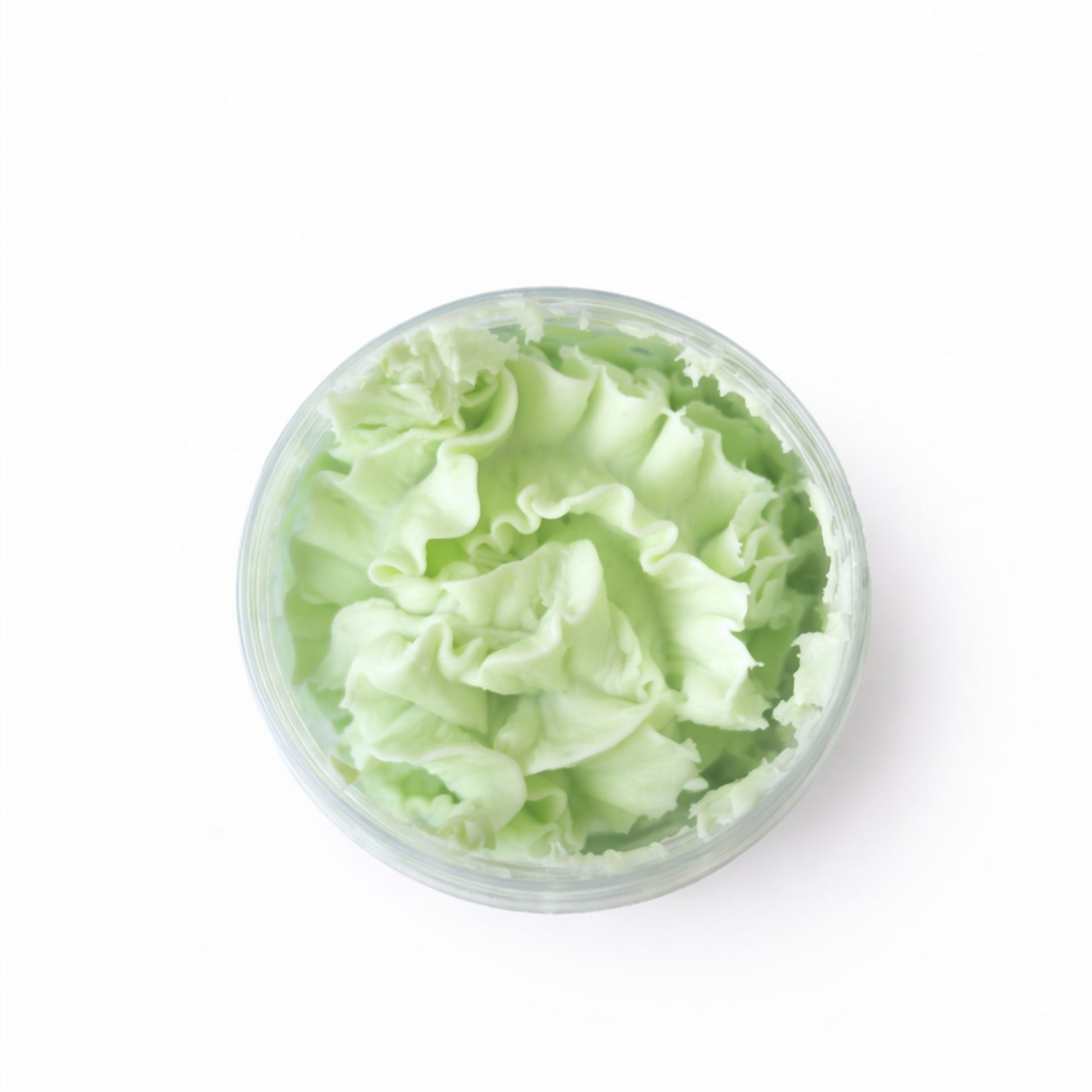 Crema facial de color verde menta en recipiente transparente, textura suave y esponjosa, ideal para hidratar la piel.
