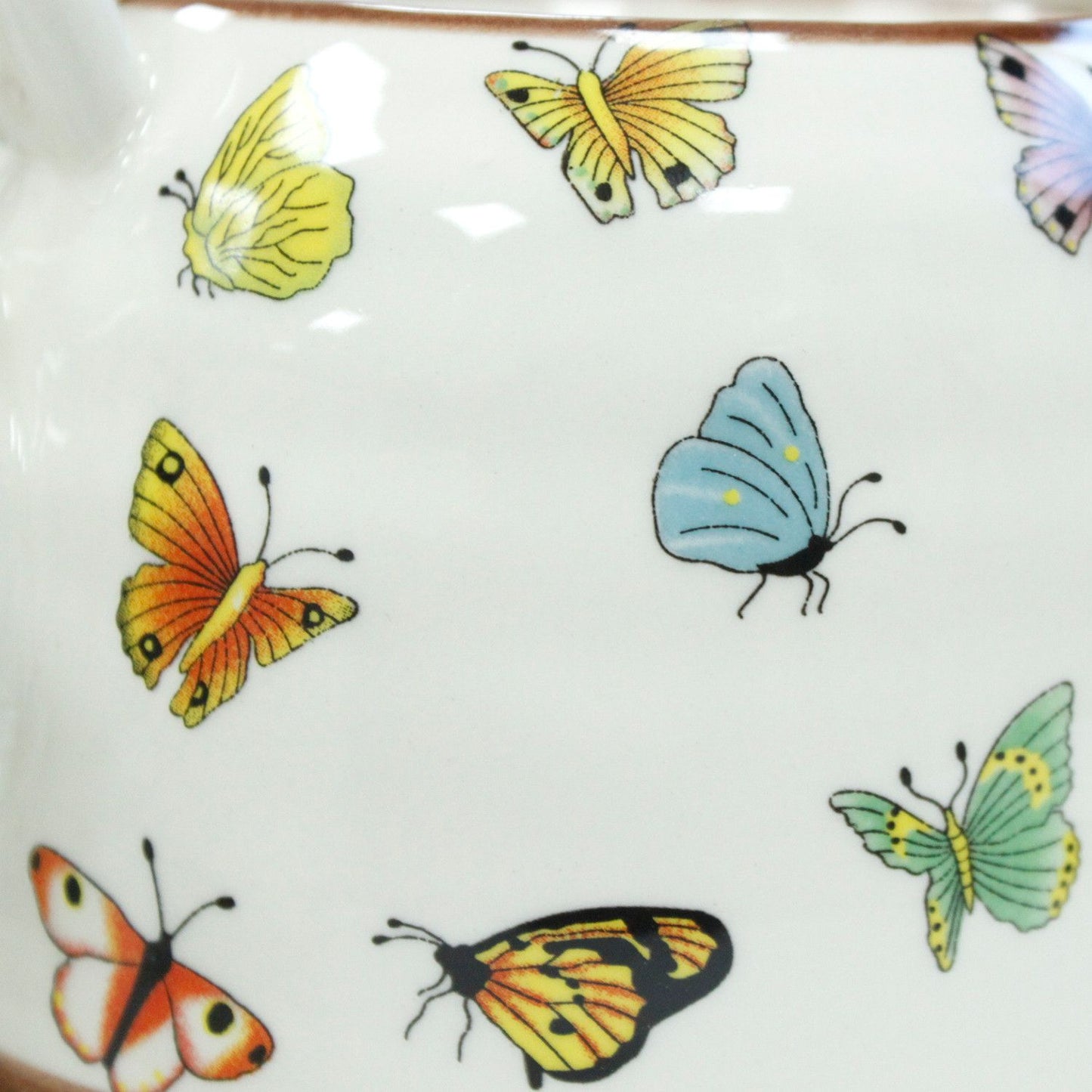 Taza de cerámica blanca con mariposas de colores brillantes: amarillas, naranjas, azules y verdes.