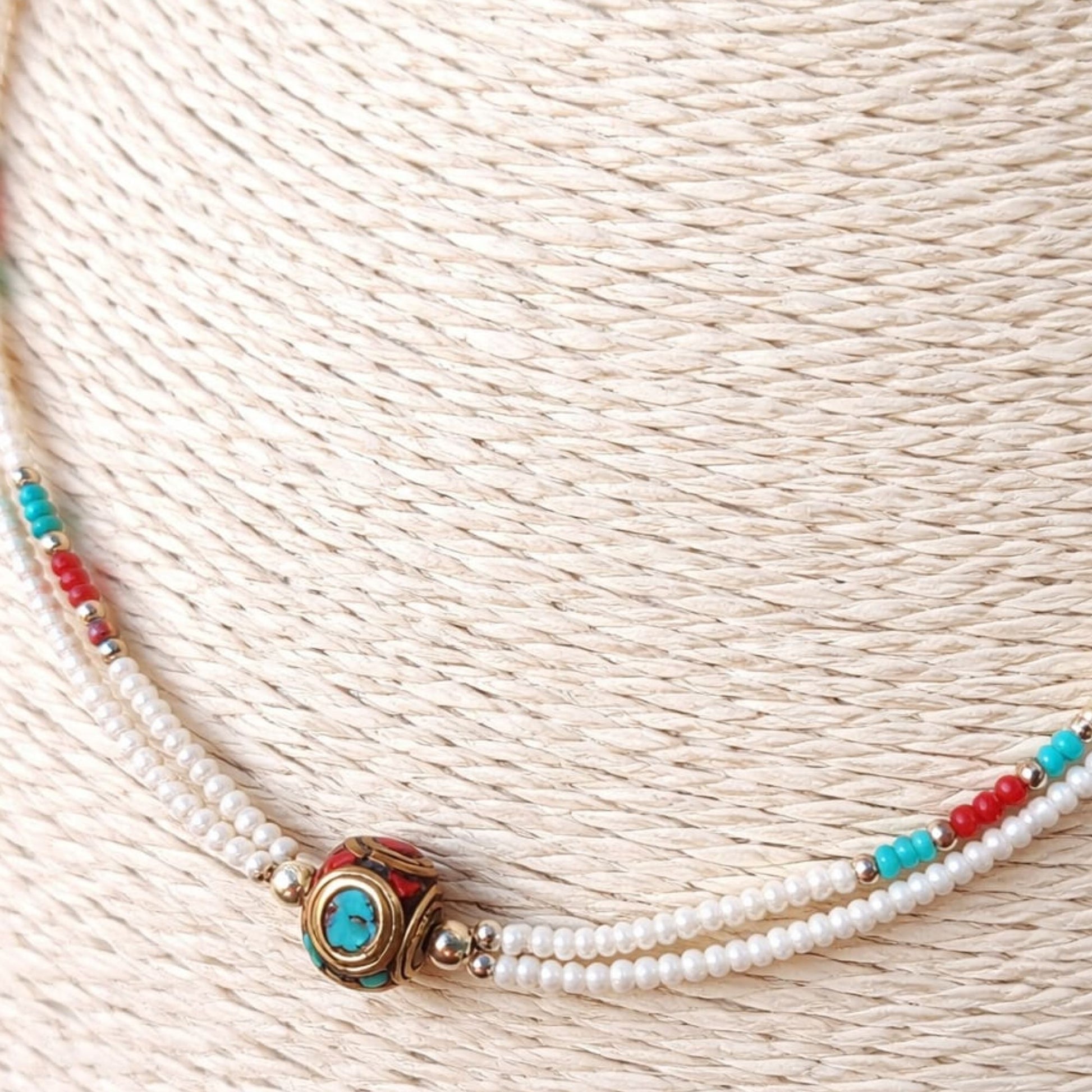 Collar de perlas blancas con detalles en turquesa y rojo, estilo bohemio y elegante.