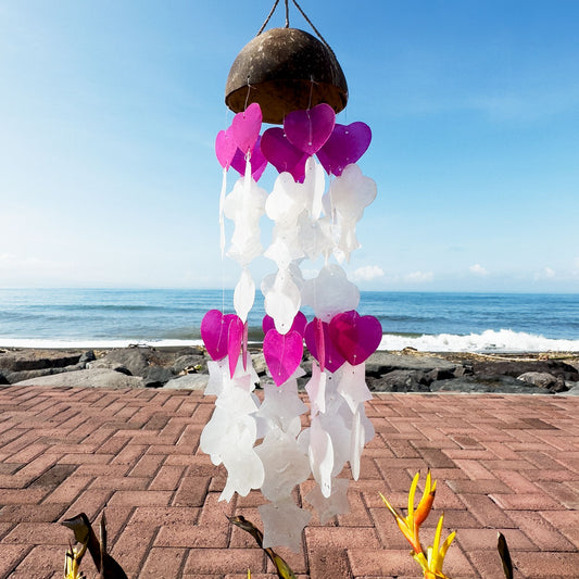 Campanas de viento de 35 cm con base de coco y colgantes de capiz en formas de corazón blancas y rosas ante el mar