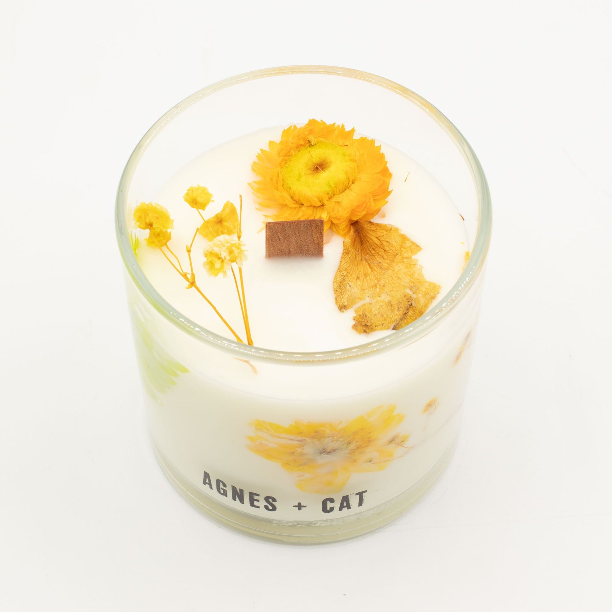 Vela aromática blanca con flores secas amarillas y naranjas en un vaso de vidrio, estilo moderno y natural.