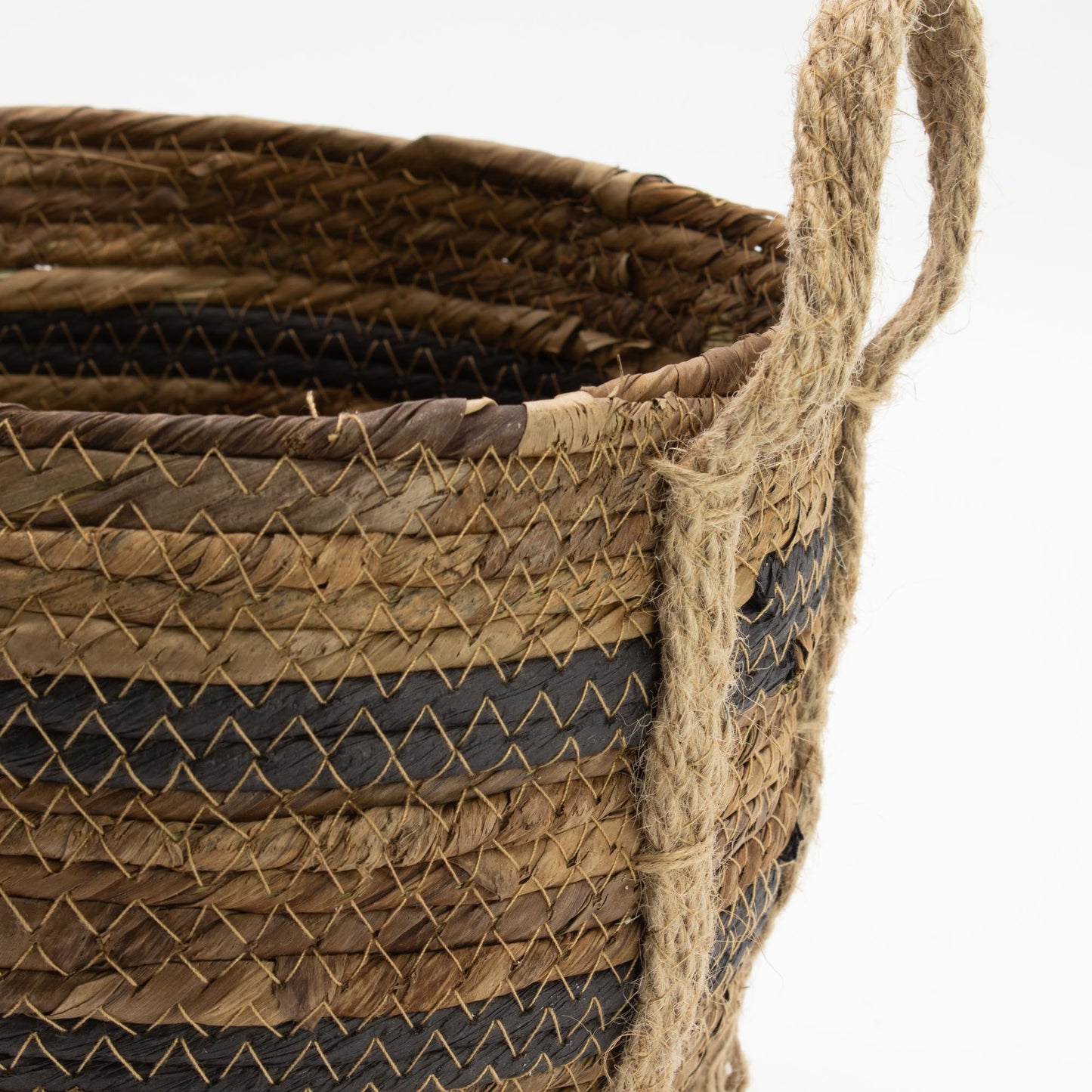 Cesta artesanal de hoja de plátano y pasto marino en tonos marrón y negro con asas de cuerda rústica.