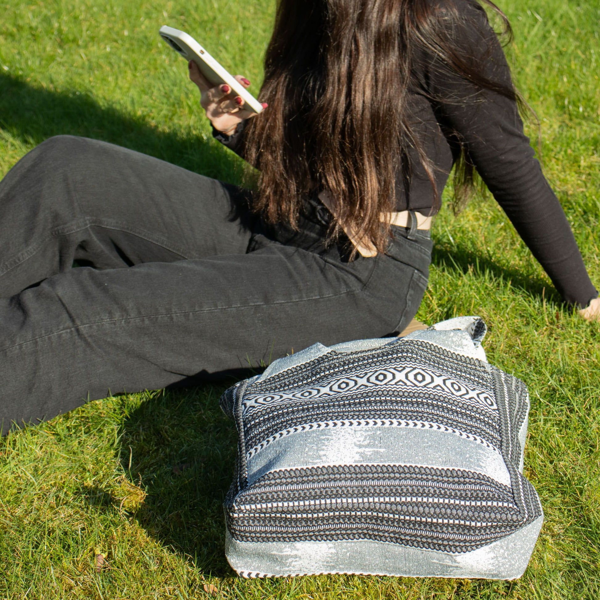 Bolso rectangular plateado y negro, con diseño étnico, ideal para uso diario, sobre césped verde.