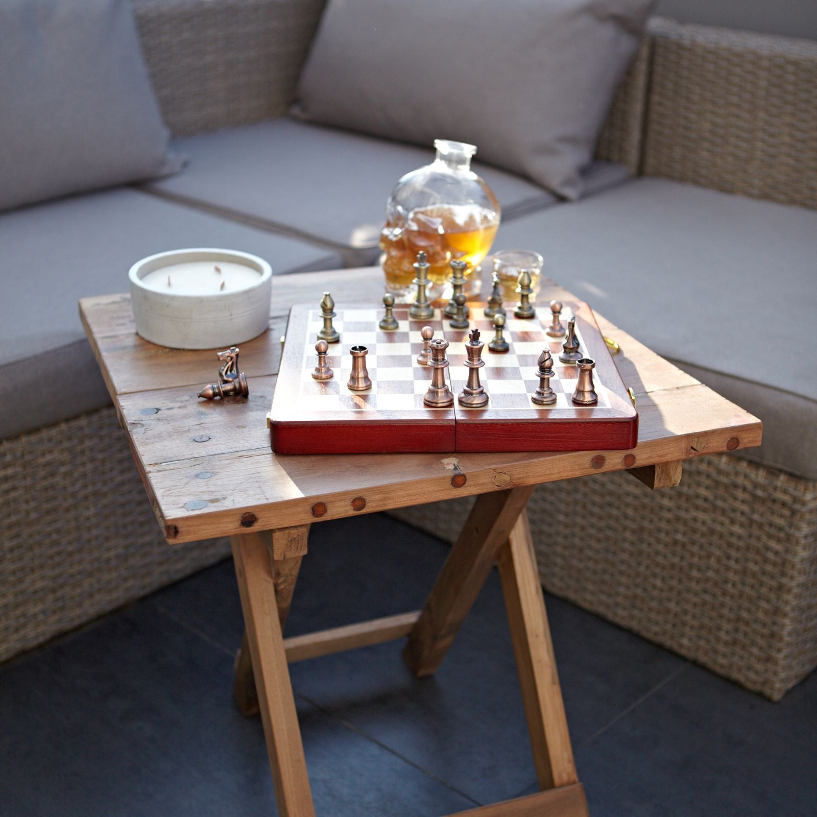 Juego de ajedrez de madera con piezas en tonos dorados y plateados, sobre mesa de madera rústica, decorado con accesorios.