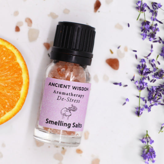 Frasco con sales rosas, junto a rodaja de naranja y flores de lavanda sobre fondo blanco. Estilo aromaterapia.