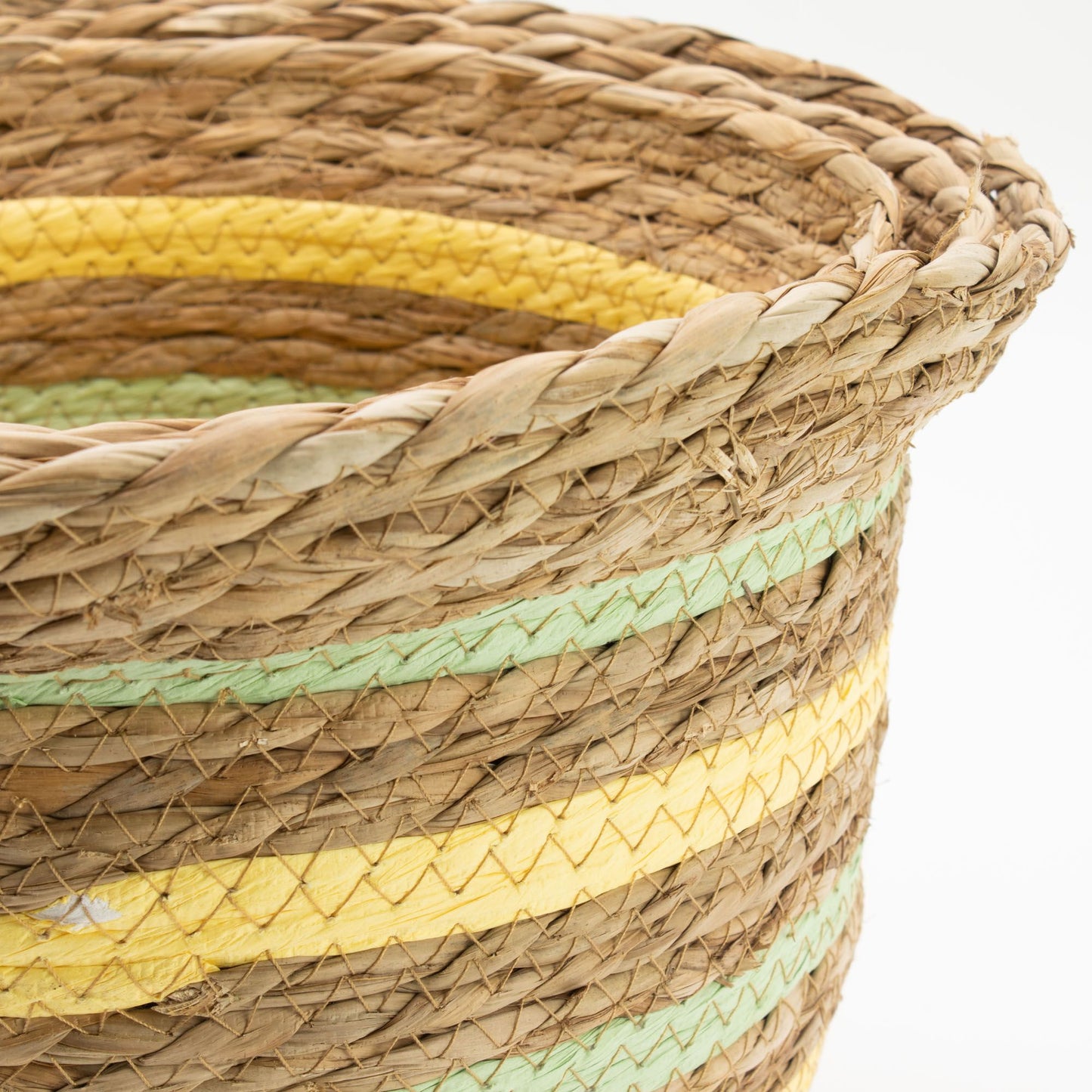 Cesta artesanal de hierba marina con texturas trenzadas, detalles de líneas horizontales en amarillo y verde claro.