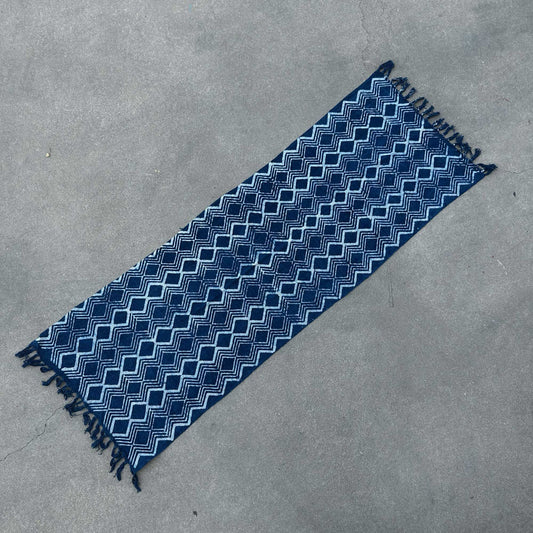 Alfombra azul marino con diseño geométrico y flecos, hecha de algodón, ideal para espacios modernos.