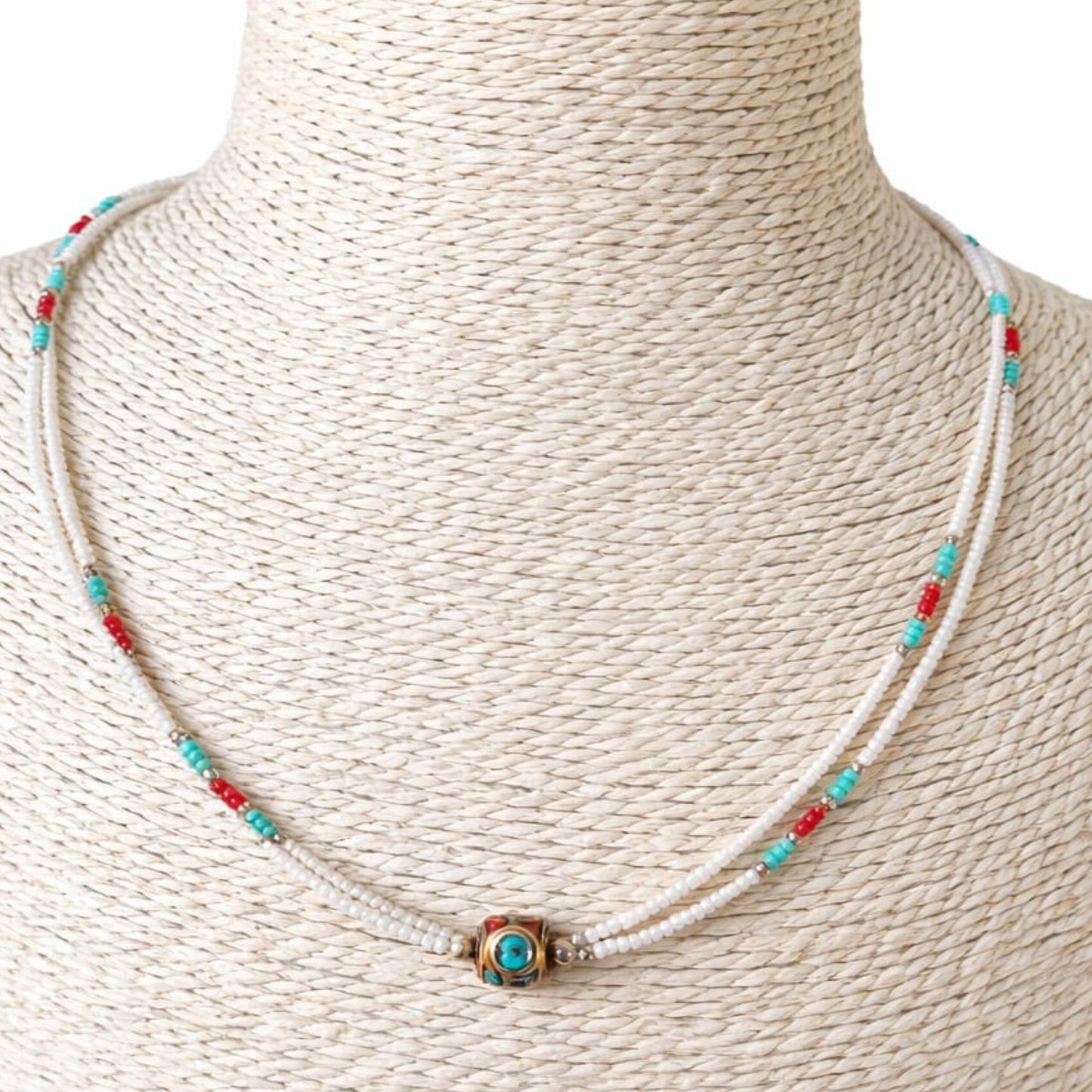 Collar de cuentas blancas, turquesas y rojas, con detalle central dorado, estilo bohemio y moderno.