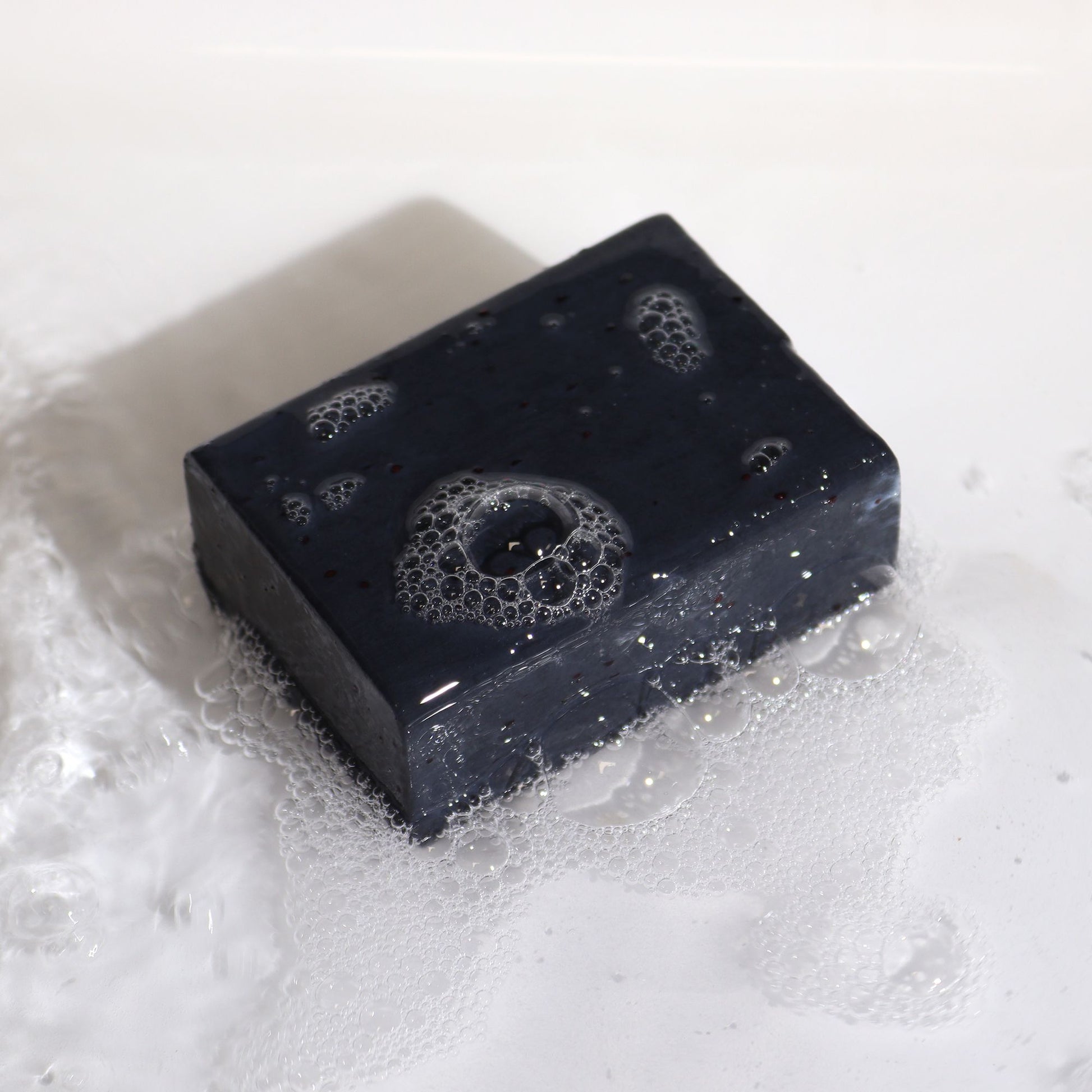 Jabón negro artesanal con burbujas, textura suave y color oscuro, ideal para limpieza profunda de la piel.